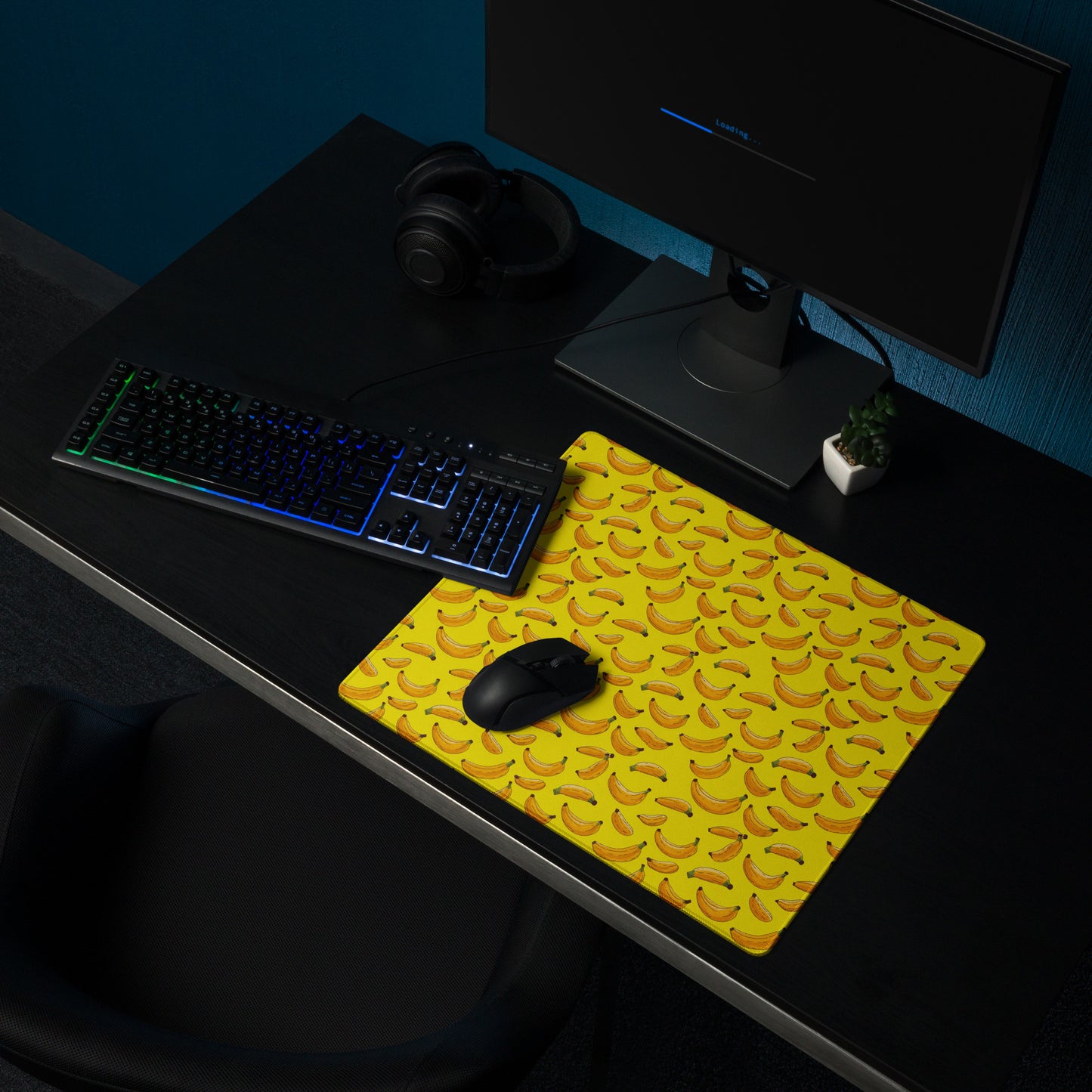 A 18" x 16" desk pad with bananas all over it shown on a desk setup. Yellow in color.