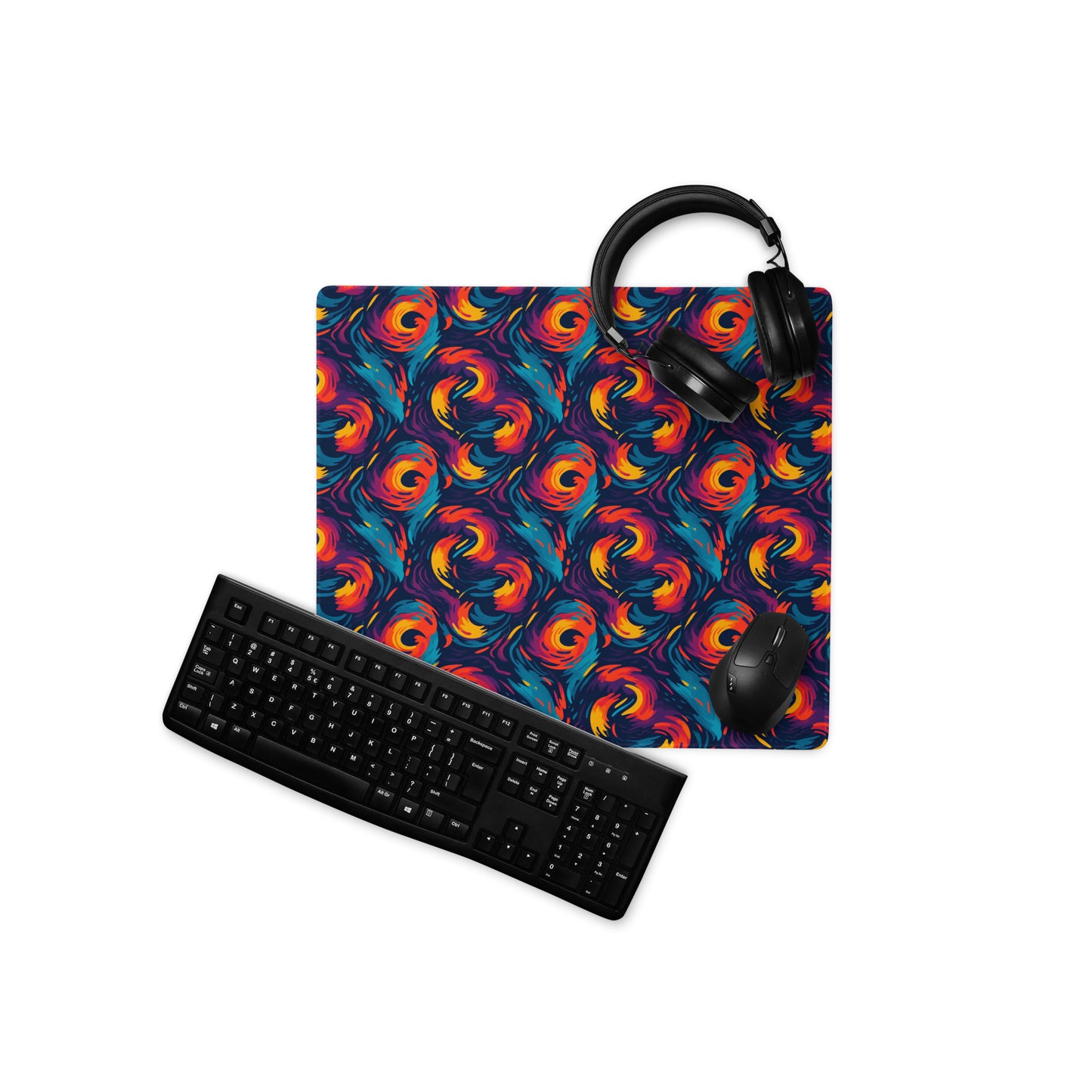 A 18" x 16" desk pad with fiery swirls on it displayed with a keyboard, headphones and a mouse. Red and Blue in color.