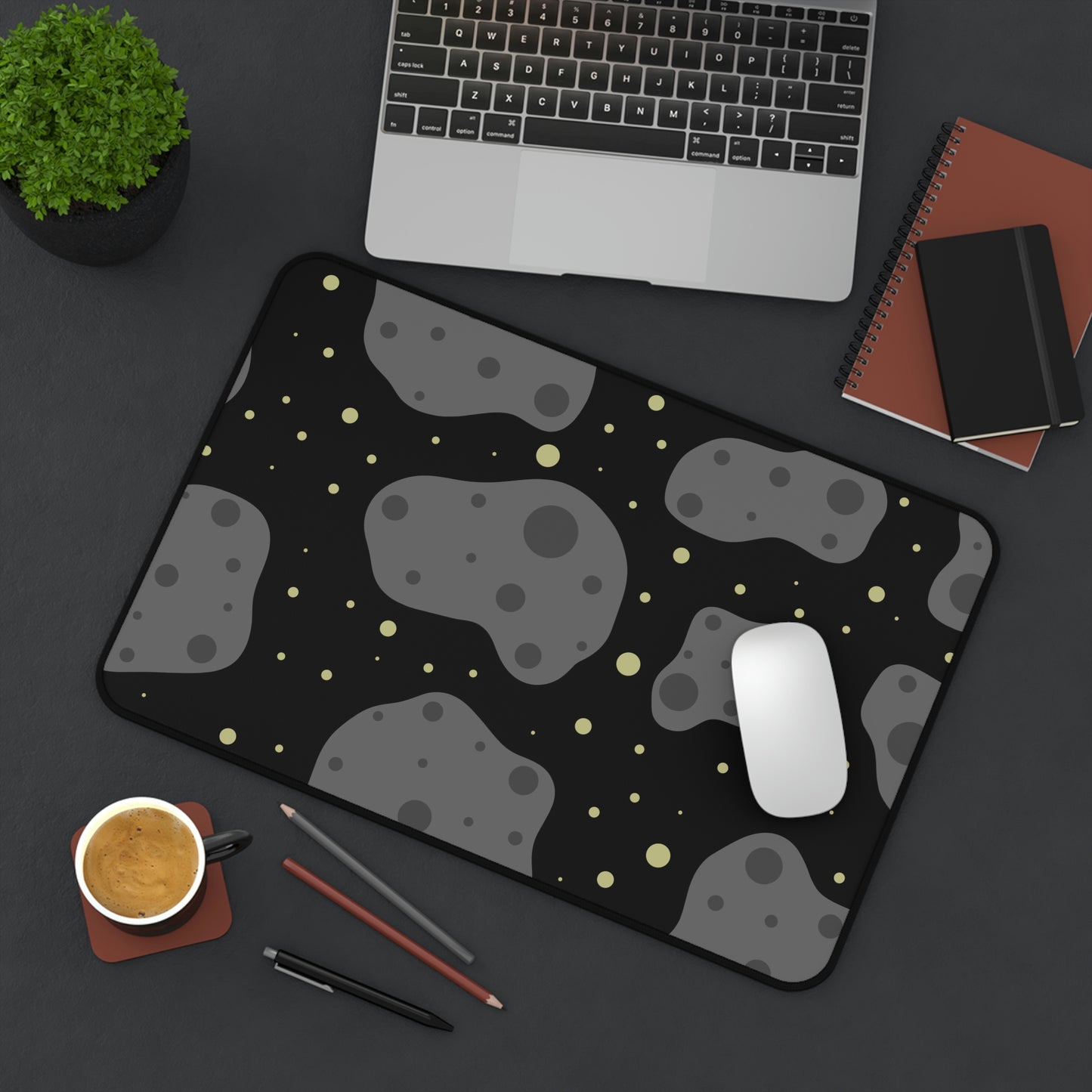 A 12" x 18" desk mat with a black background, gray asteroids, and yellow stars sitting at an angle.