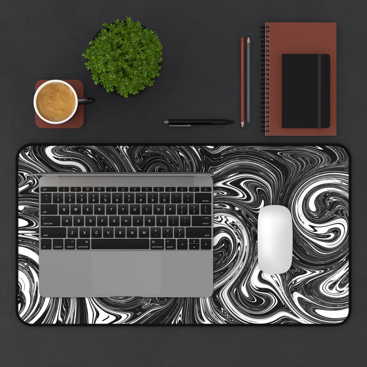 A 12" x 22" desk mat with black and white swirls. A laptop and mouse sit on top of it.
