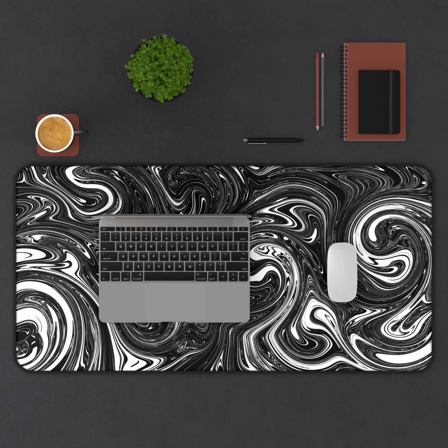 A 31" x 15.5" desk mat with black and white swirls. A laptop and mouse sit on top of it.