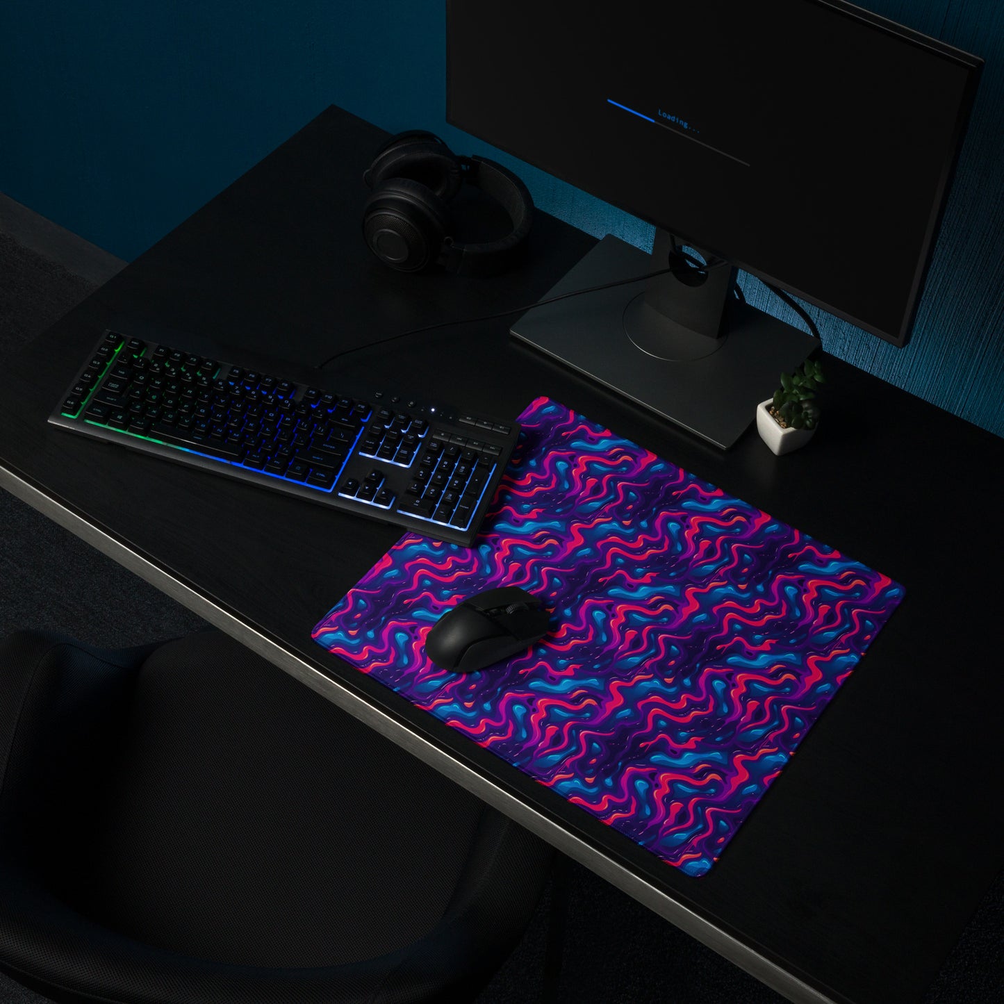 A 18" x 16" desk pad with a pink, blue and purple wavy pattern sitting on a desk.