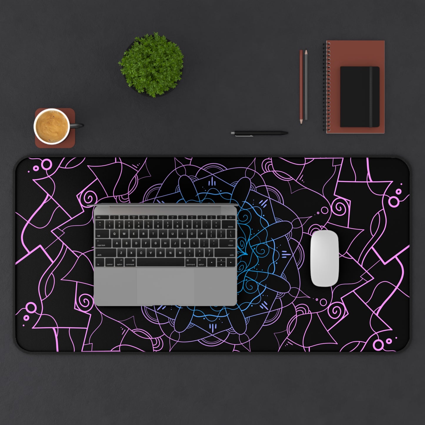 A 31" x 15.5" desk mat with a pink and blue mandala pattern on a black background. A laptop and mouse sit on top of it.