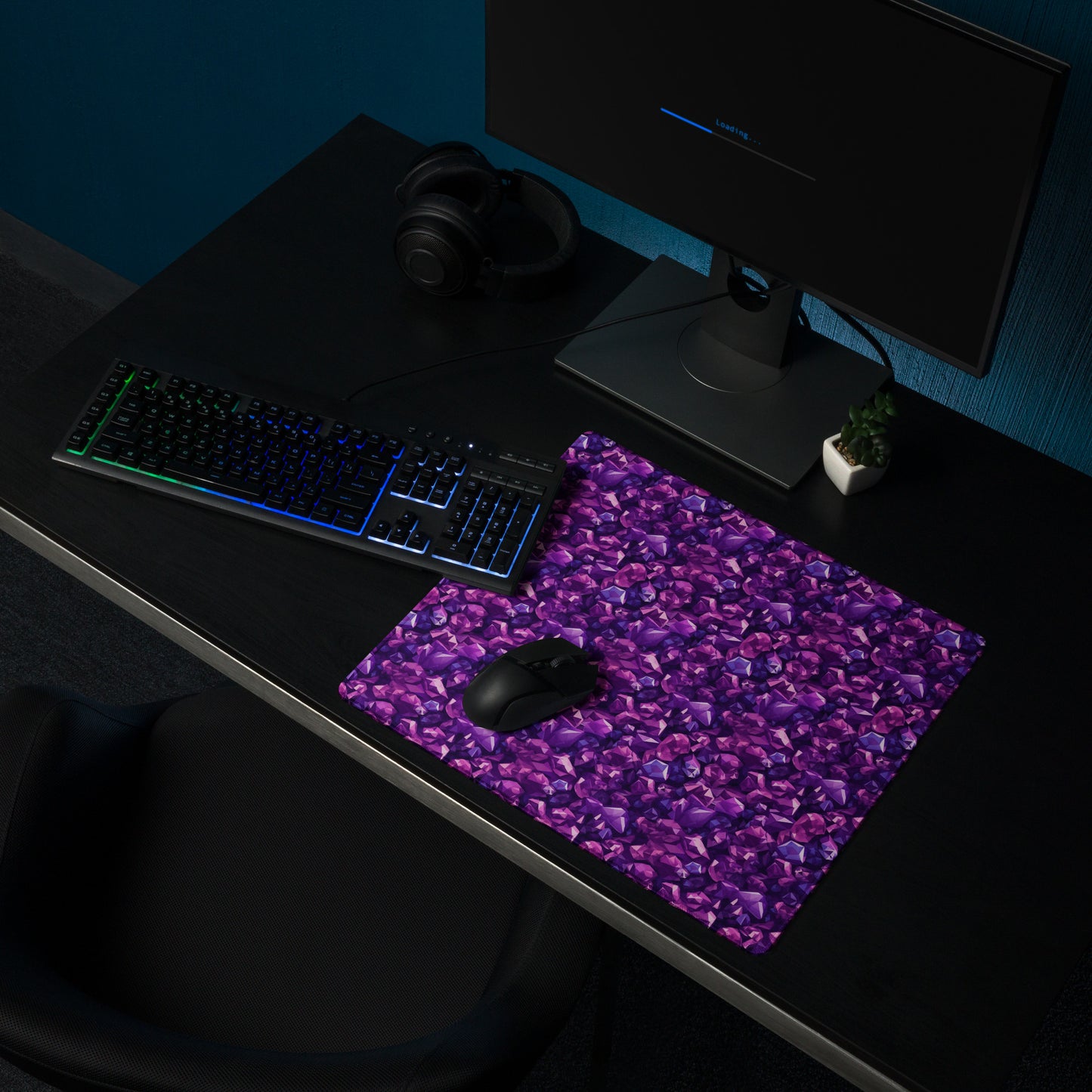 An 18" x 16" gaming desk pad with purple crystals. It sits on a black desk with a monitor, keyboard, and mouse.