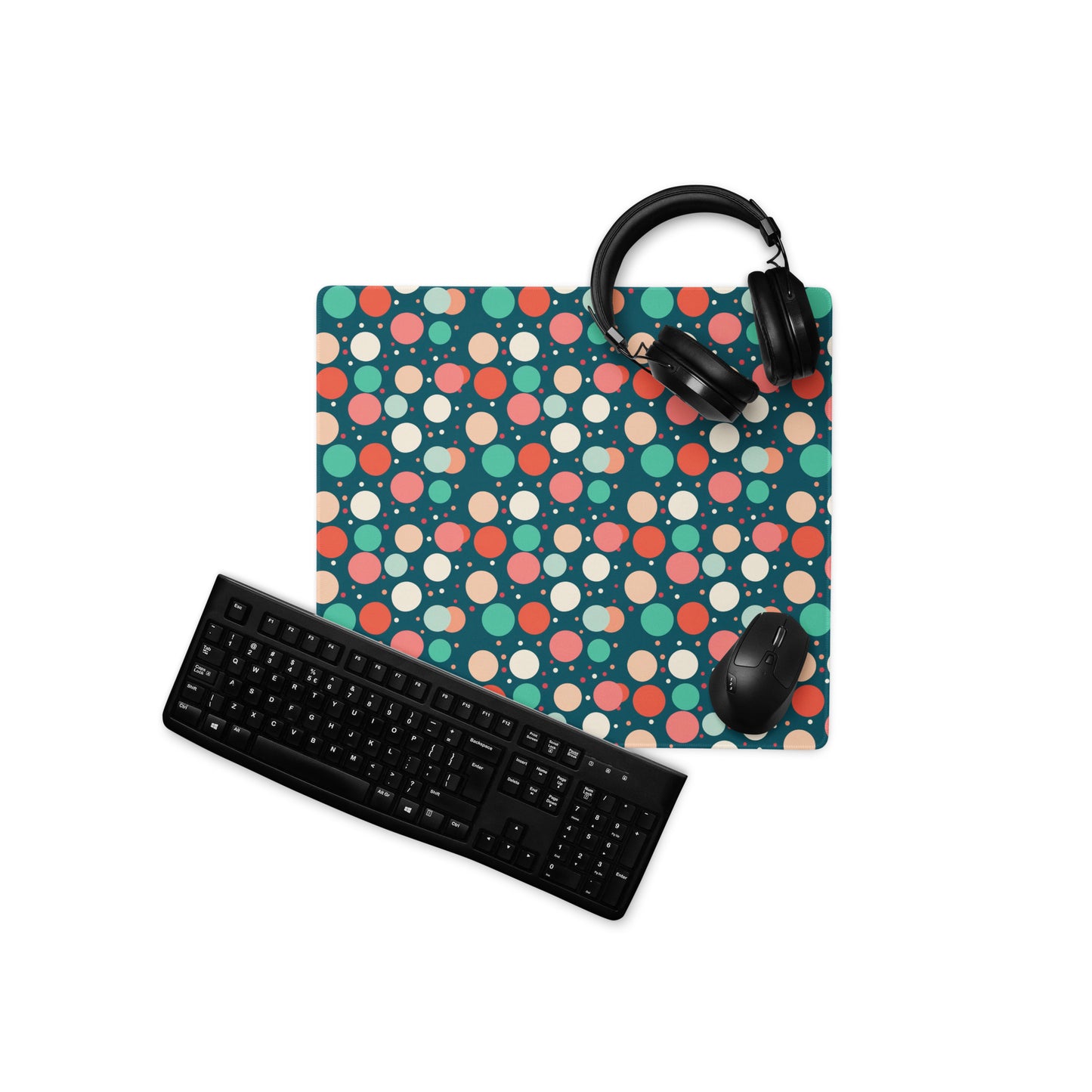 A 18" x 16" desk pad with red teal and yellow polka dot pattern. With a keyboard, mouse, and headphones sitting on it.