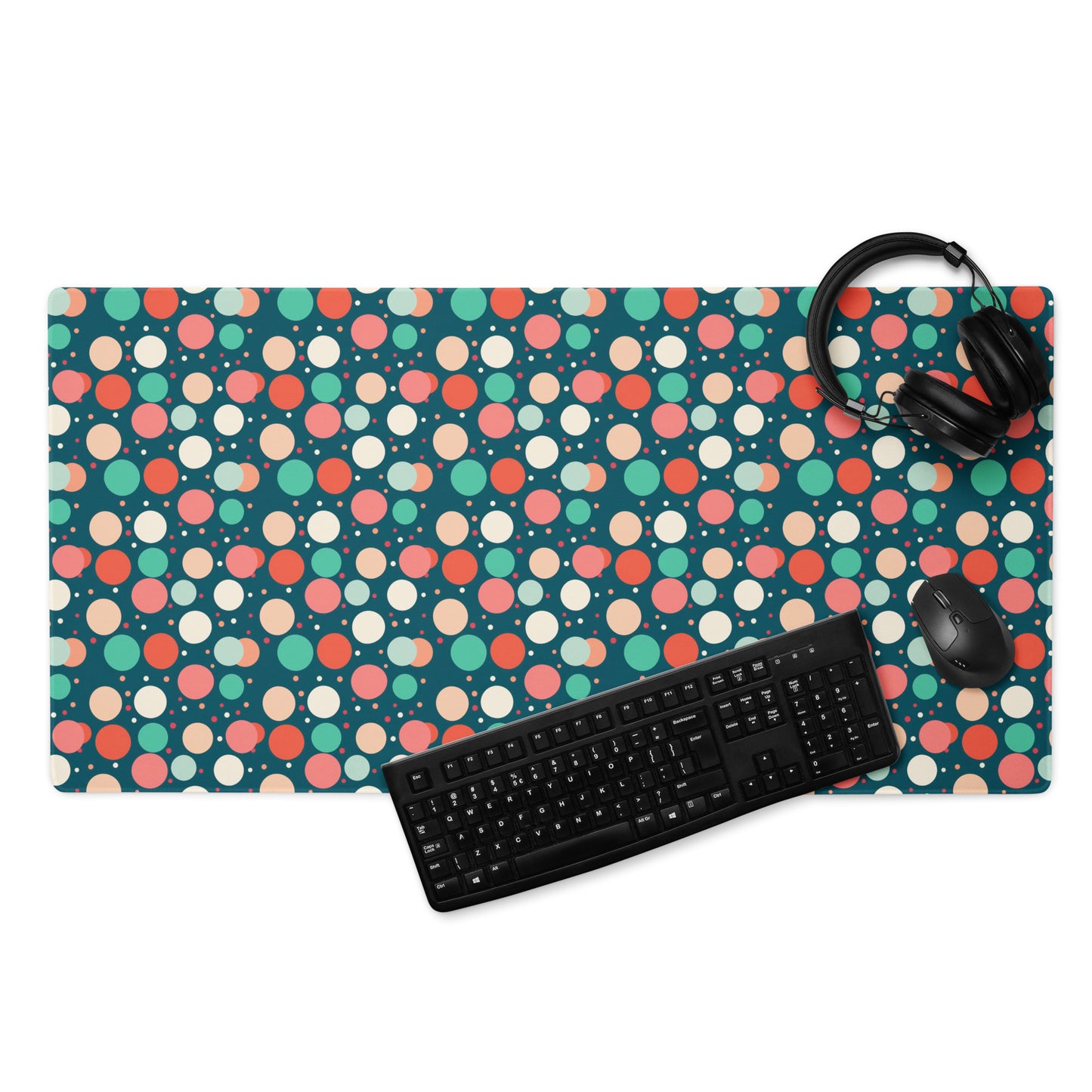 A 36" x 18" desk pad with red teal and yellow polka dot pattern. With a keyboard, mouse, and headphones sitting on it.
