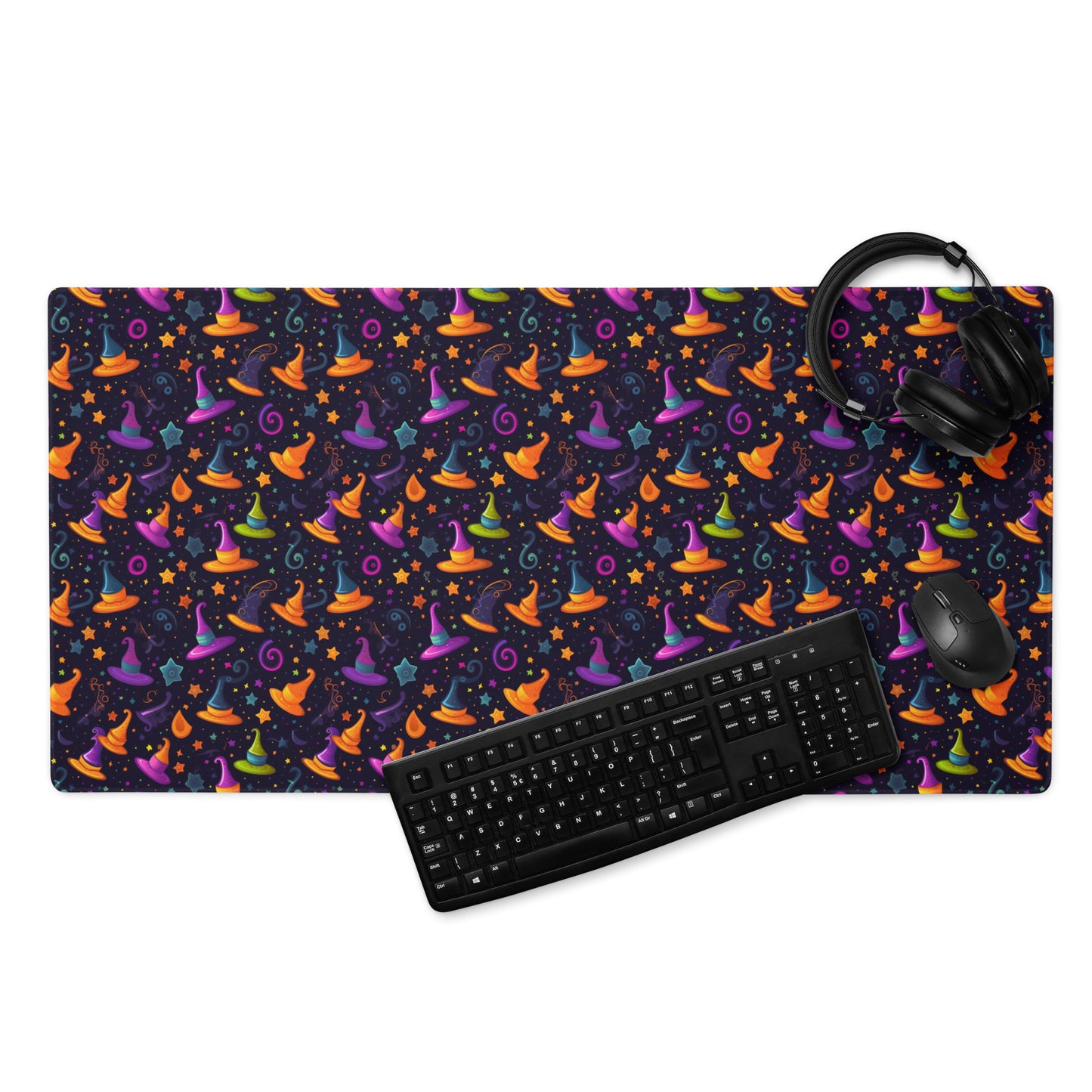 A 36" x 18" desk pad with a orange and purple wizard hat pattern. With a keyboard, mouse, and headphones sitting on it.