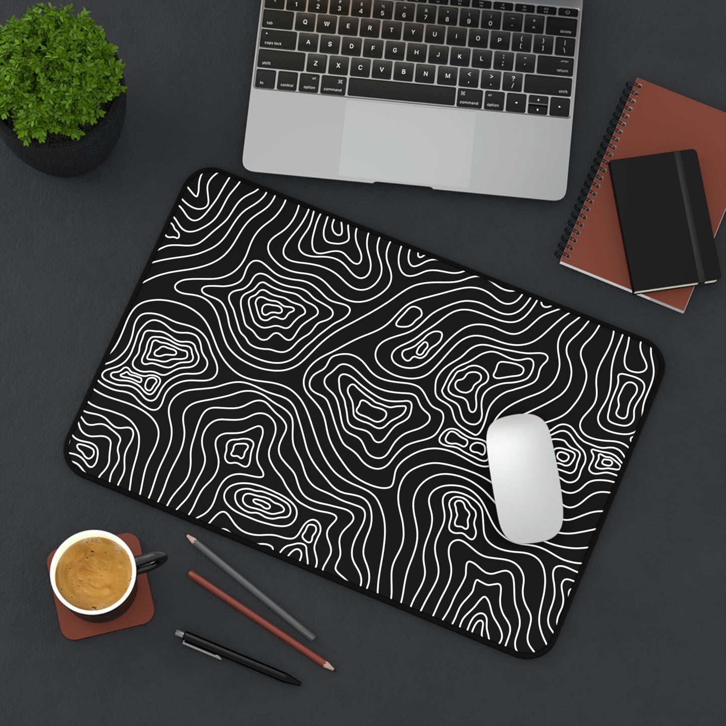 A 12" x 18" black desk mat with white topographic lines sitting at an angle. A mouse sits on top of it.