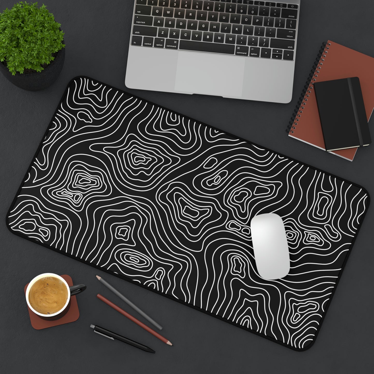 A 12" x 22" black desk mat with white topographic lines sitting at an angle. A mouse sits on top of it.