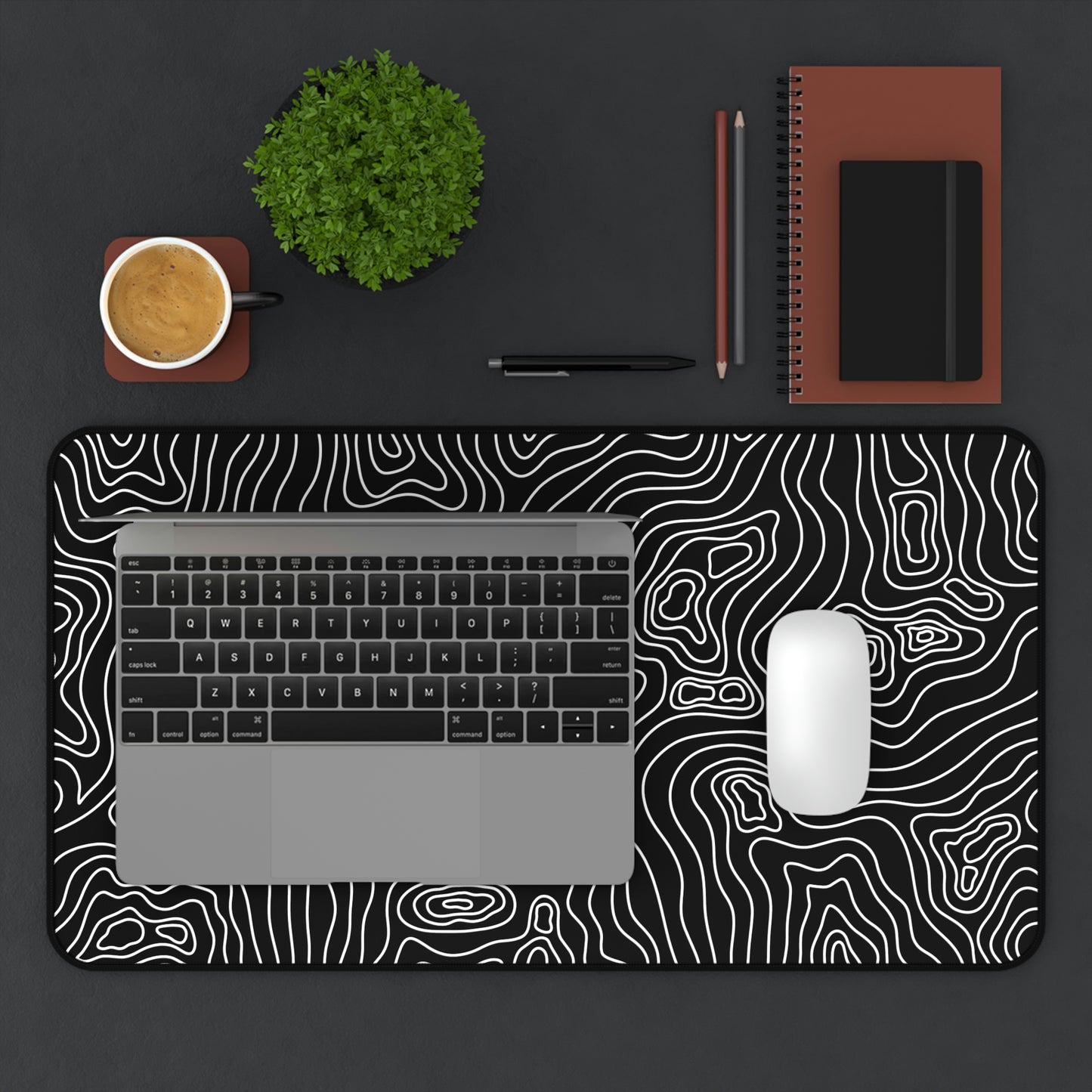 A 12" x 22" black desk mat with white topographic lines. A laptop and mouse sit on top of it.