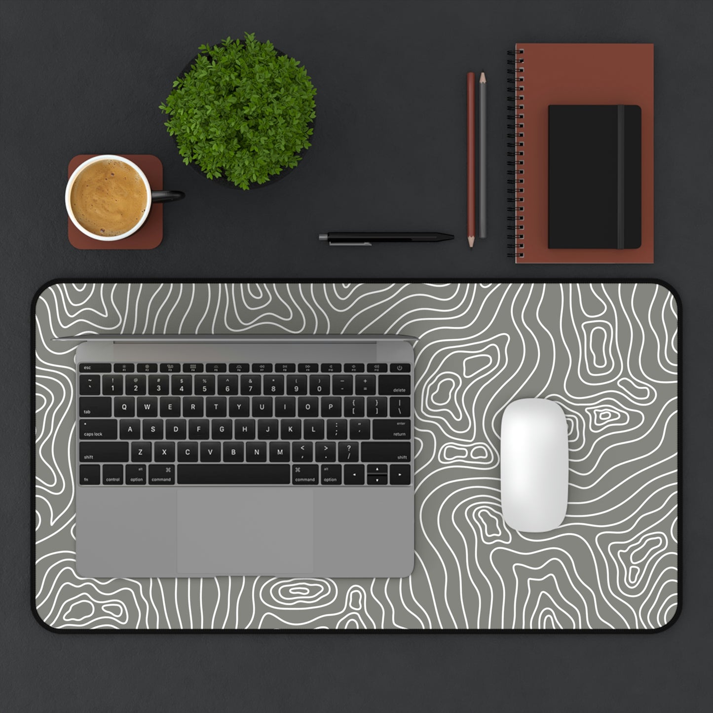 A 12" x 22" gray desk mat with white topographic lines. A laptop and mouse sit on top of it.