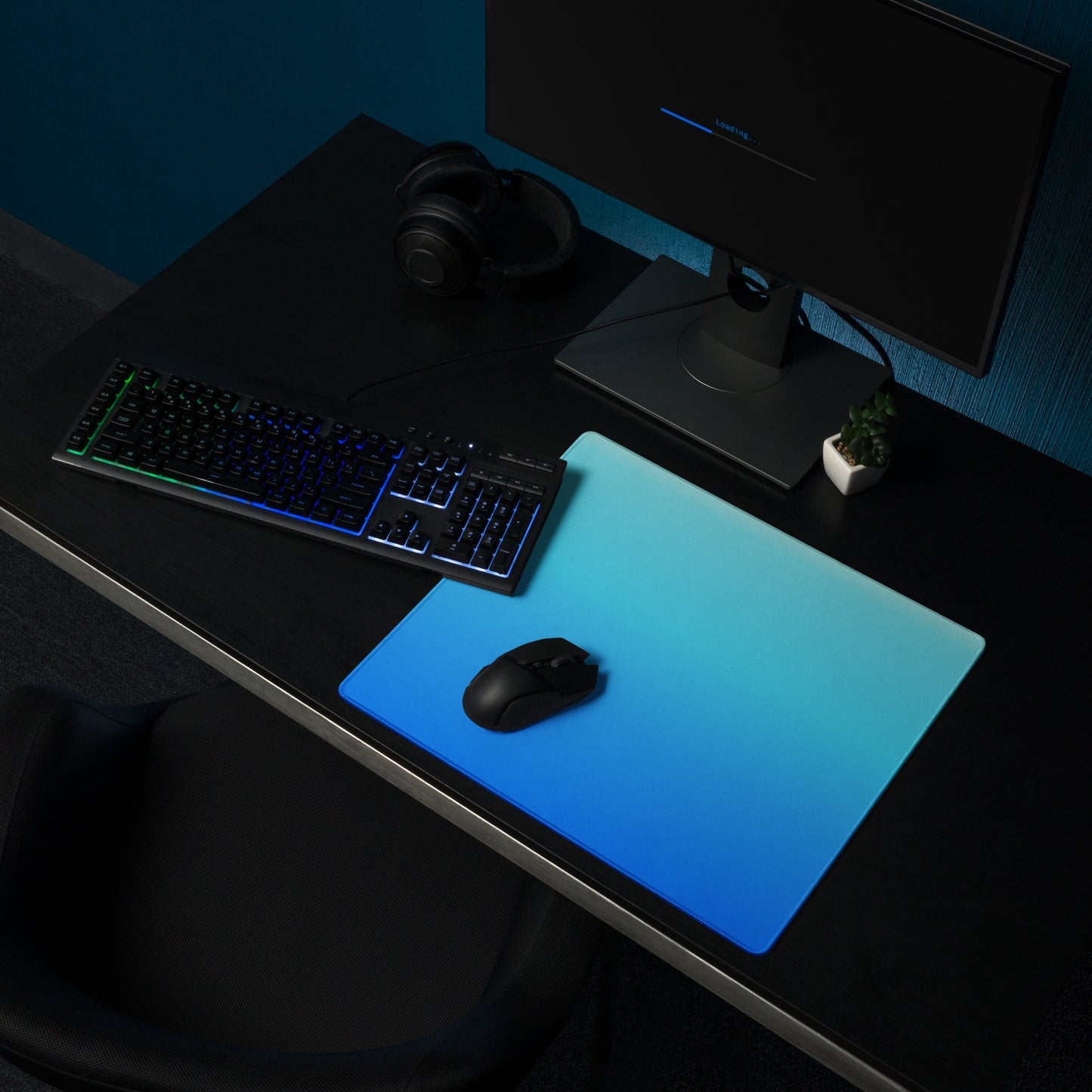 An 18" x 16" gaming desk pad with dark blue at the bottom and light blue at the top. It sits on a desk with a monitor, keyboard, and mouse.