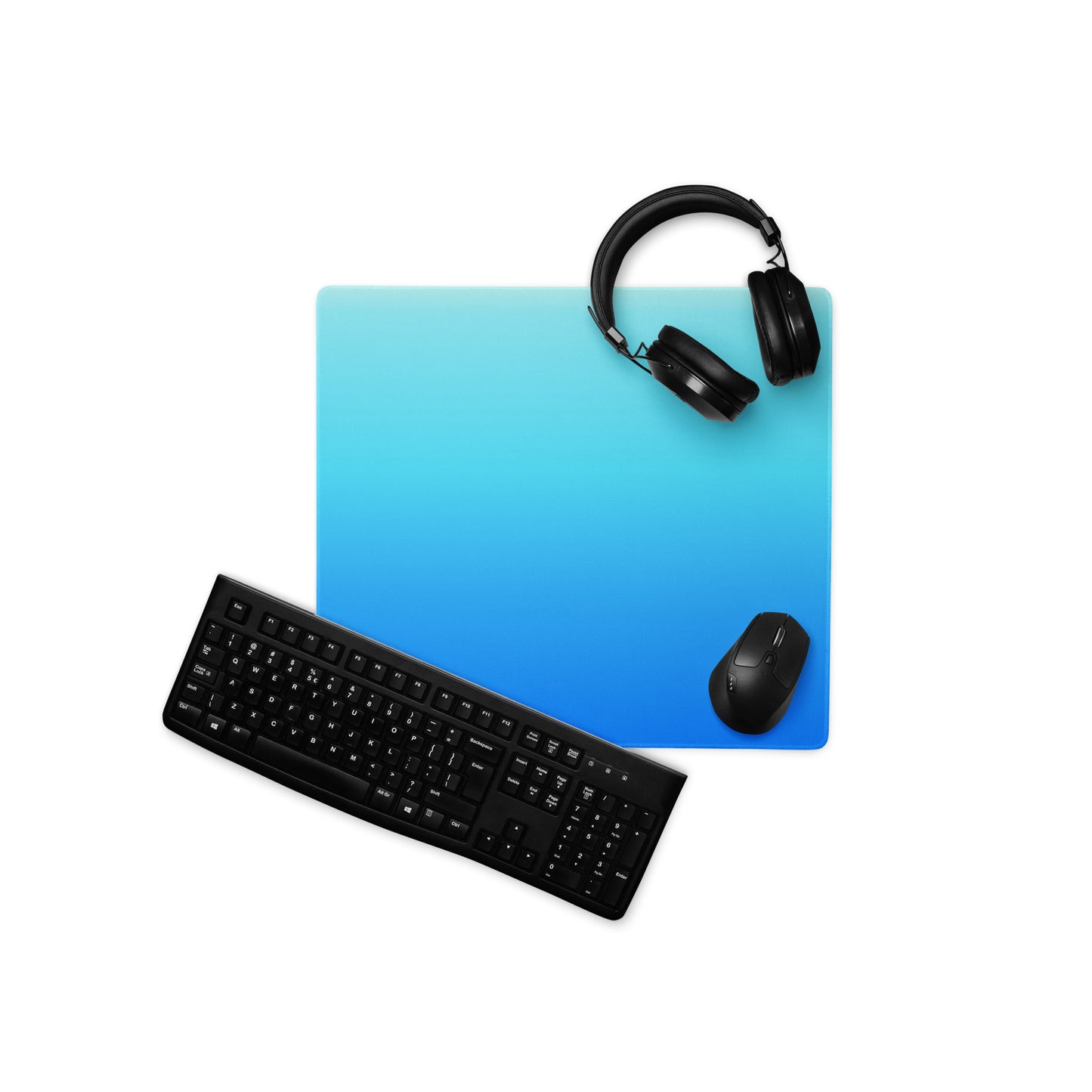 An 18" x 16" gaming desk pad with dark blue at the bottom and light blue at the top. A keyboard, headphones, and mouse sit on top of it.