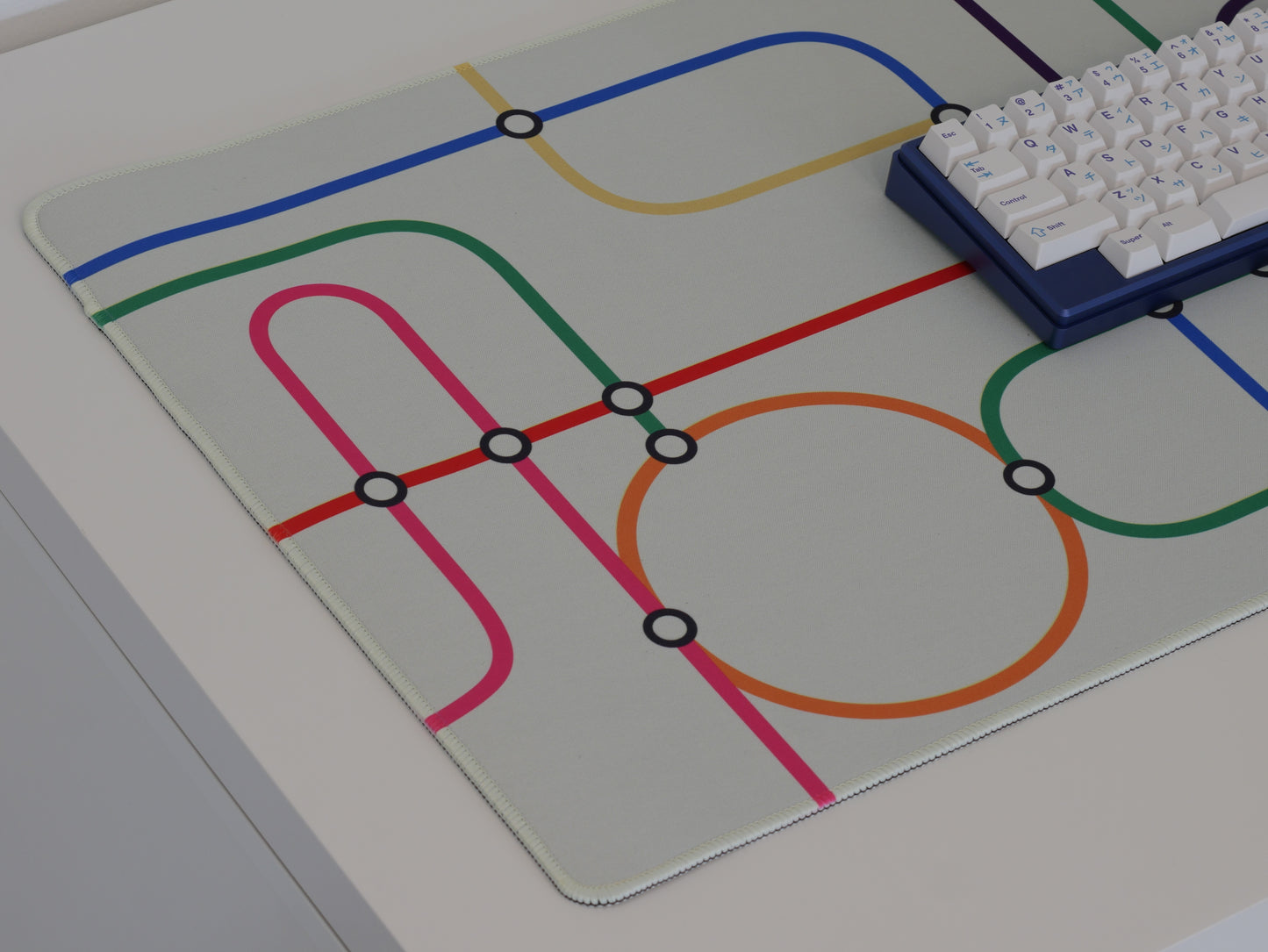 The left side of the subway transit desk mat. The desk mat has a white background and colorful lines.