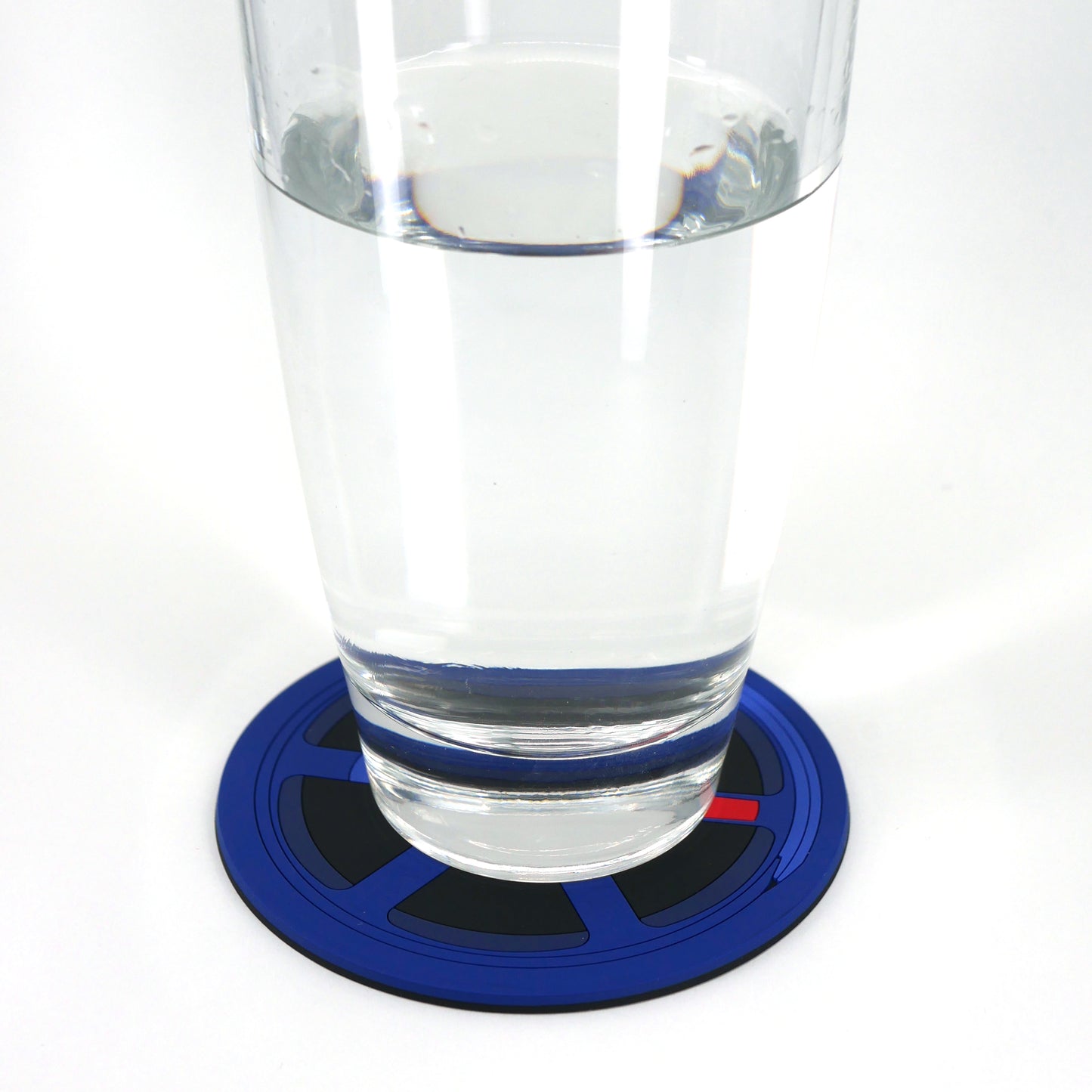 A glass of water sitting on a blue TE wheel PVC rubber coaster.