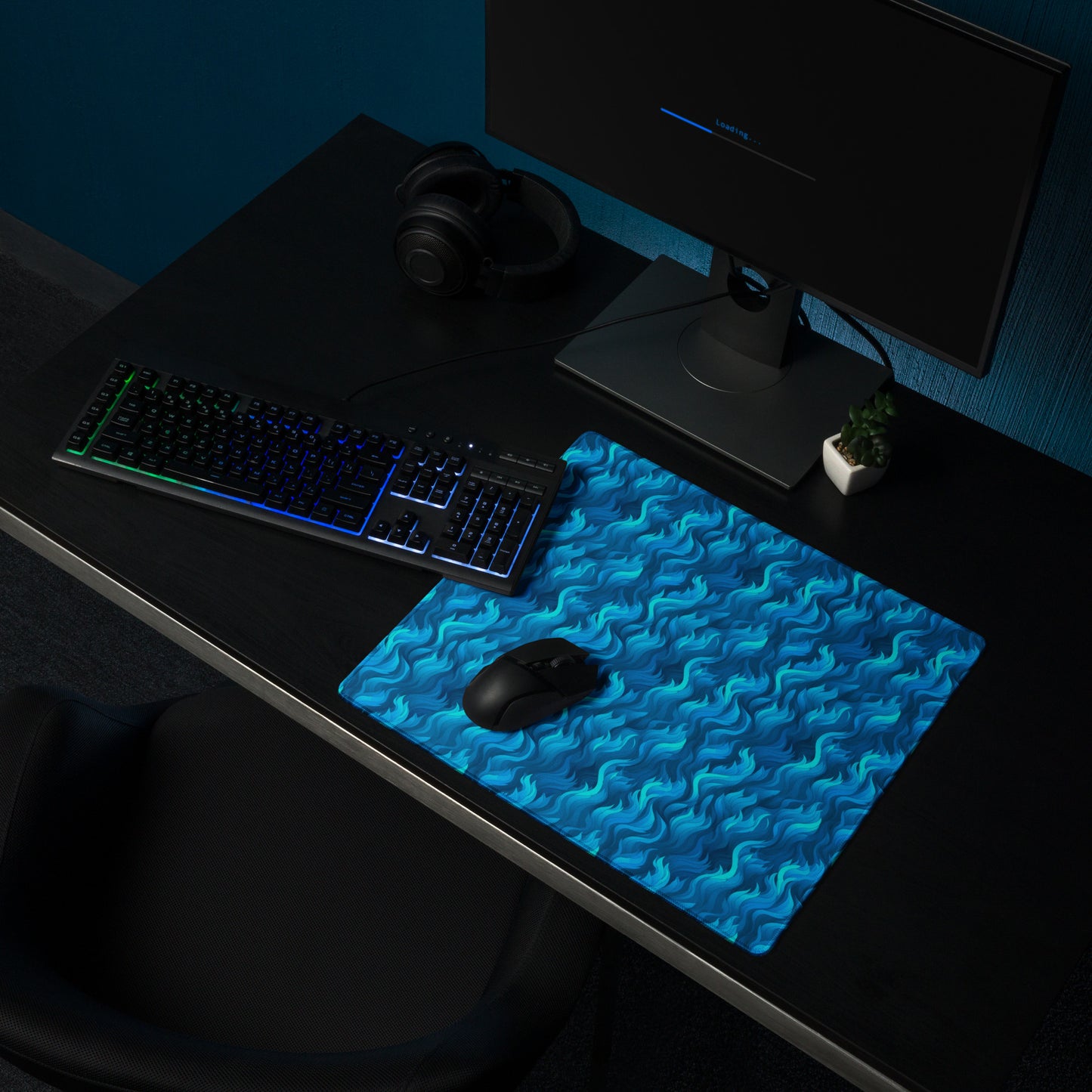 A 18" x 16" desk pad with a wavy flame pattern on it shown on a desk setup. Blue in color.