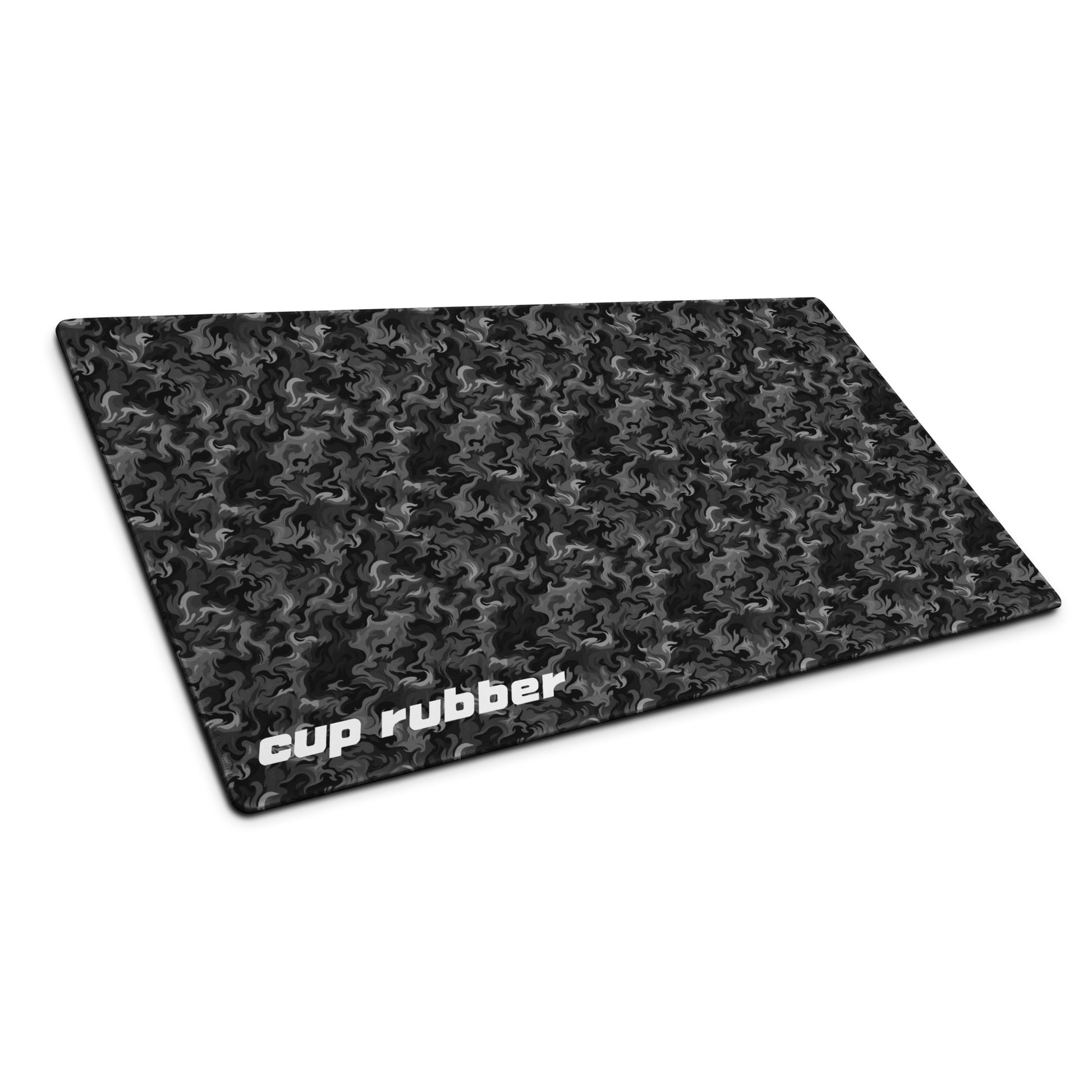 A 36" x 18" desk pad with a camo pattern all over it and the word "Cup Rubber" in the bottom left corner shown at an angle. Black and Charcoal in color.