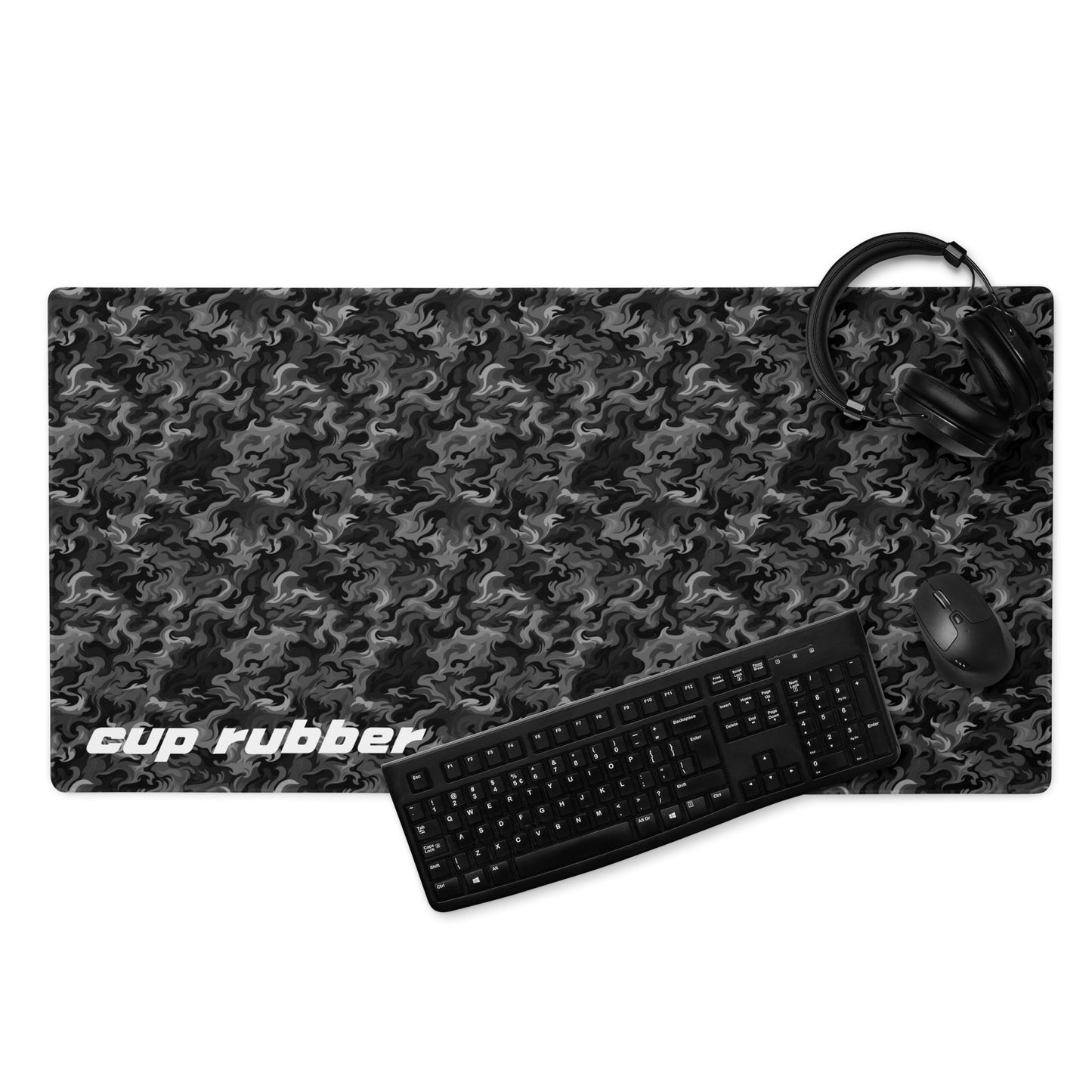A 36" x 18" desk pad with a camo pattern all over it and the word "Cup Rubber" in the bottom left corner displayed with a keyboard, headphones and a mouse. Black and Charcoal in color.