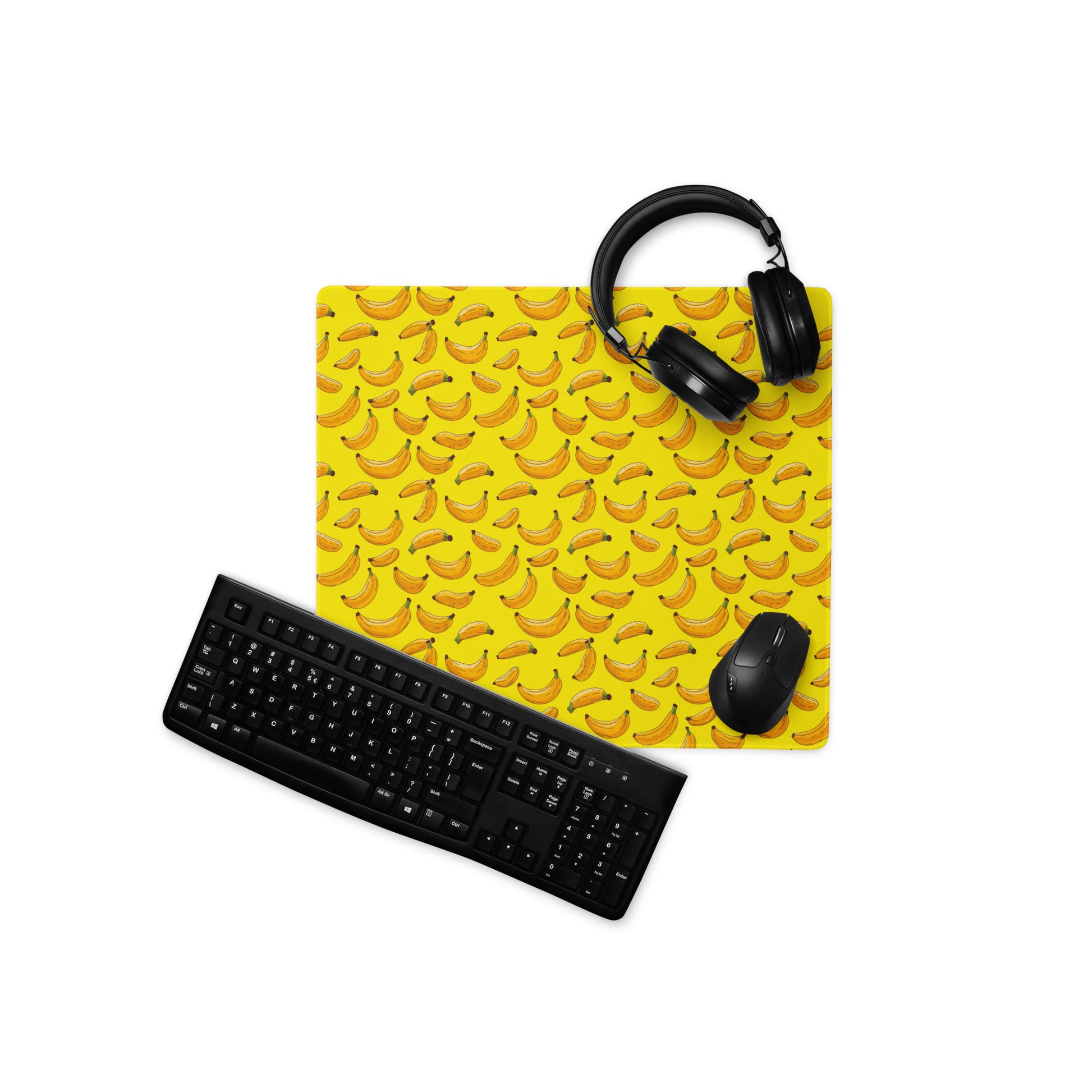 A 18" x 16" desk pad with bananas all over it displayed with a keyboard, headphones and a mouse on it. Yellow in color.