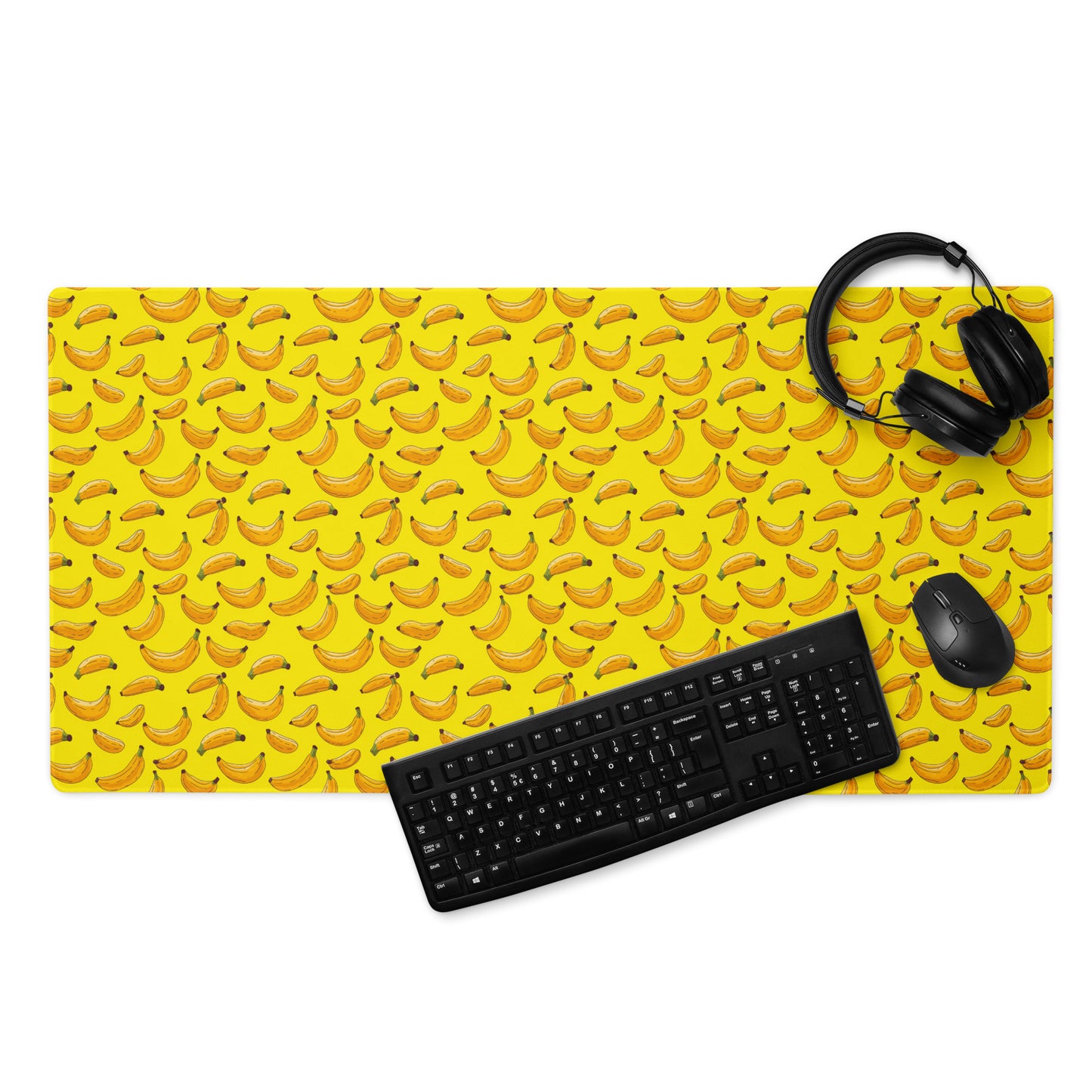 A 36" x 18" desk pad with bananas all over it displayed with a keyboard, headphones and a mouse on it. Yellow in color.