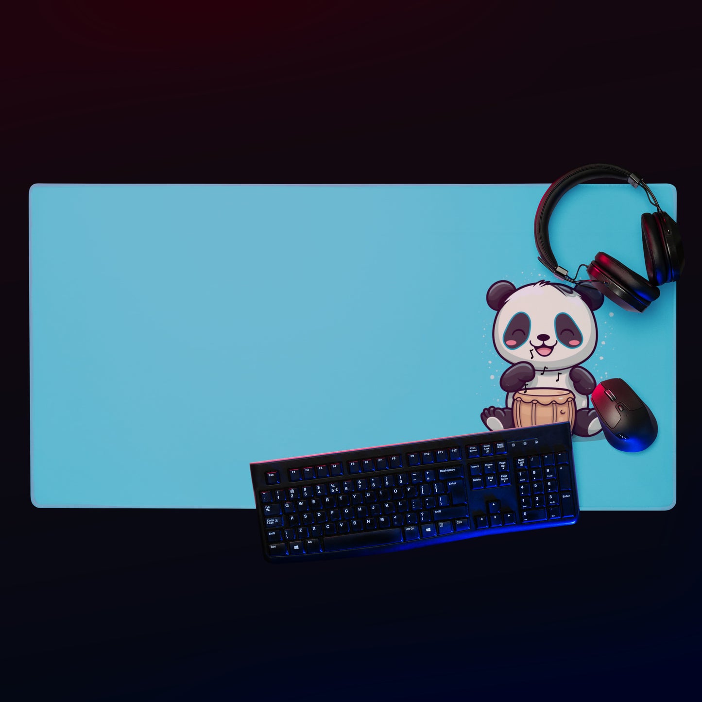 A 36" x 18" desk pad with a cute panda playing the bongos on the right displayed with  headphones, a keyboard and a mouse on it. Blue in color.