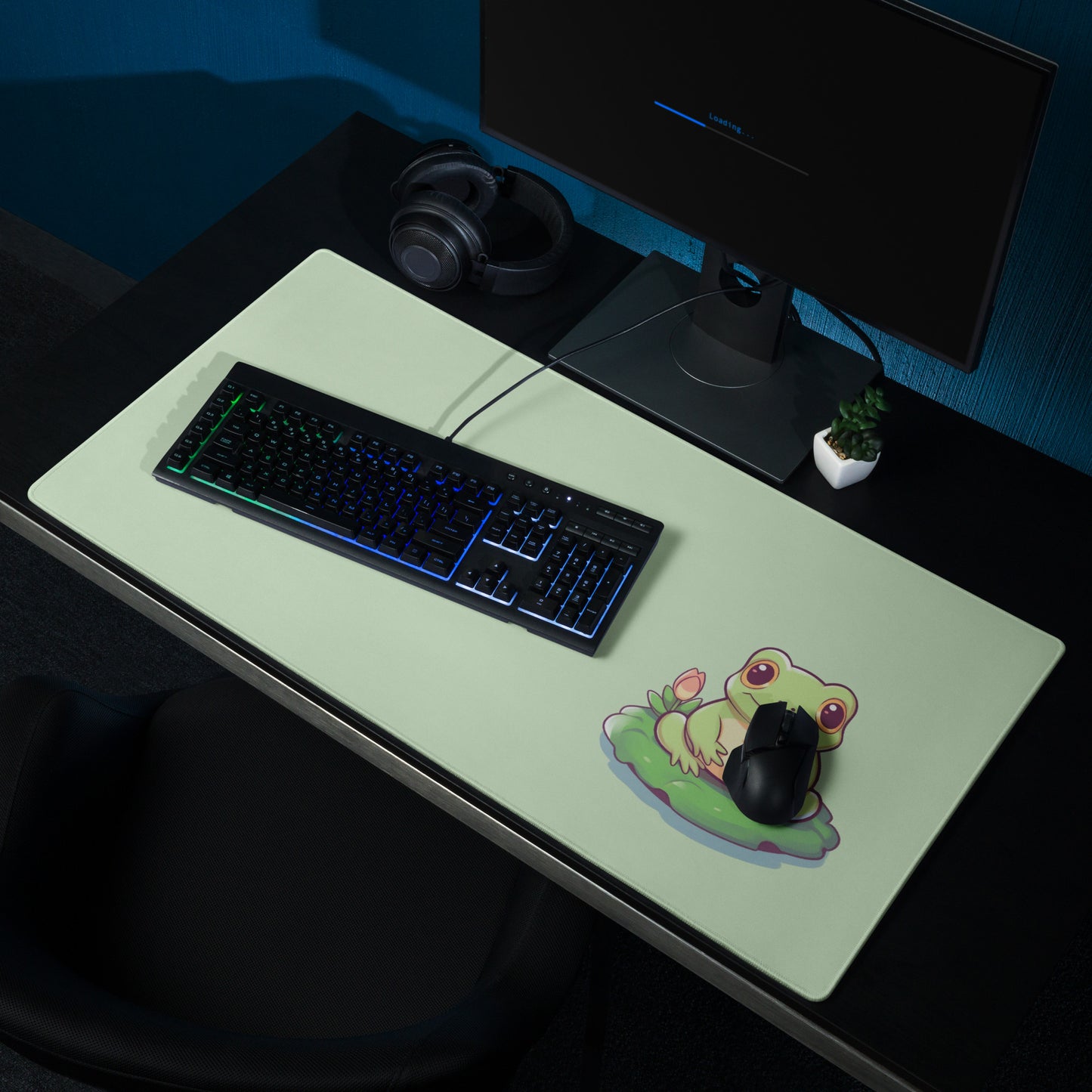 A 36" x 18" desk pad with a cute frog on it shown on a desk setup. Green in color.