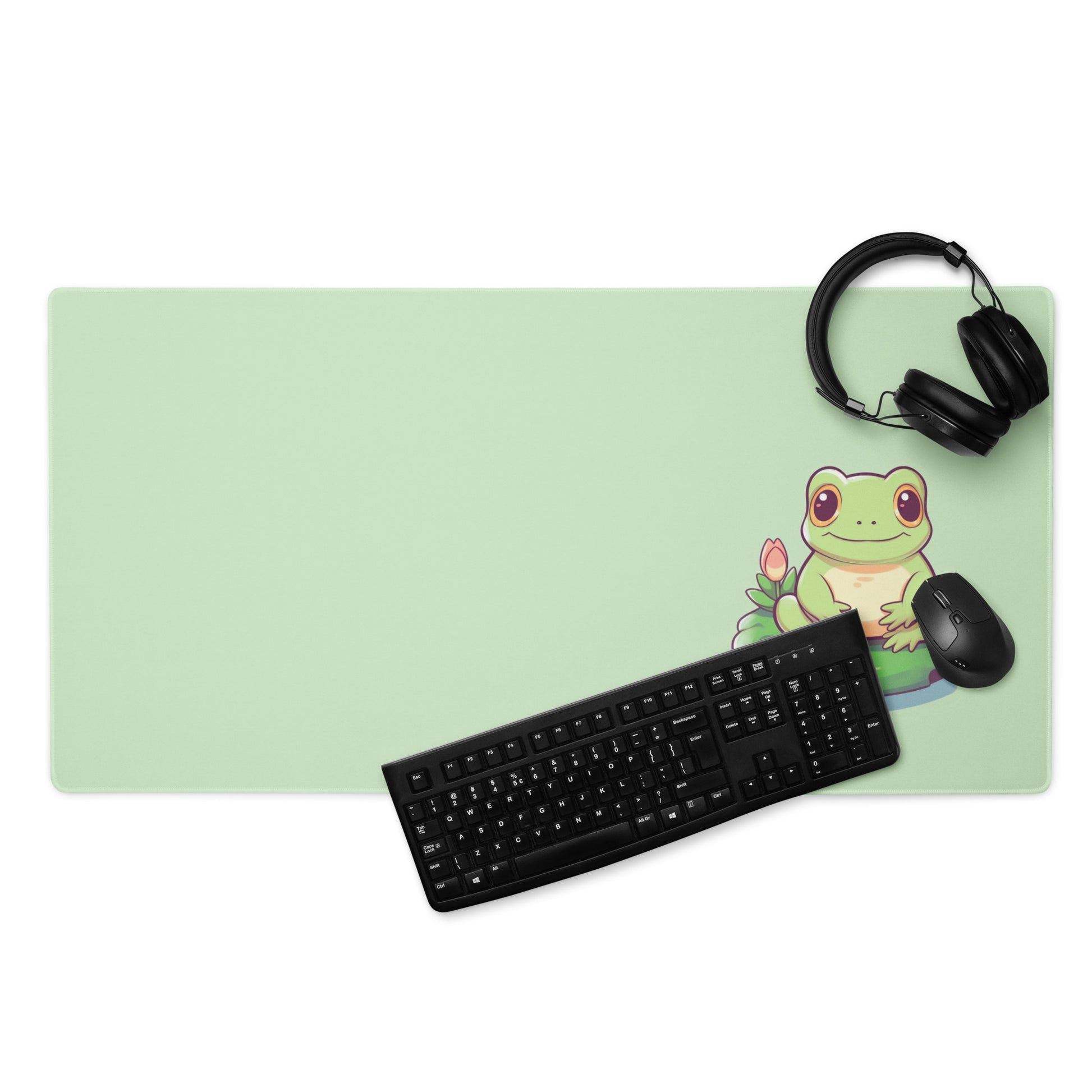 A 36" x 18" desk pad with a cute frog on it displayed with a keyboard, headphones and a mouse. Green in color.