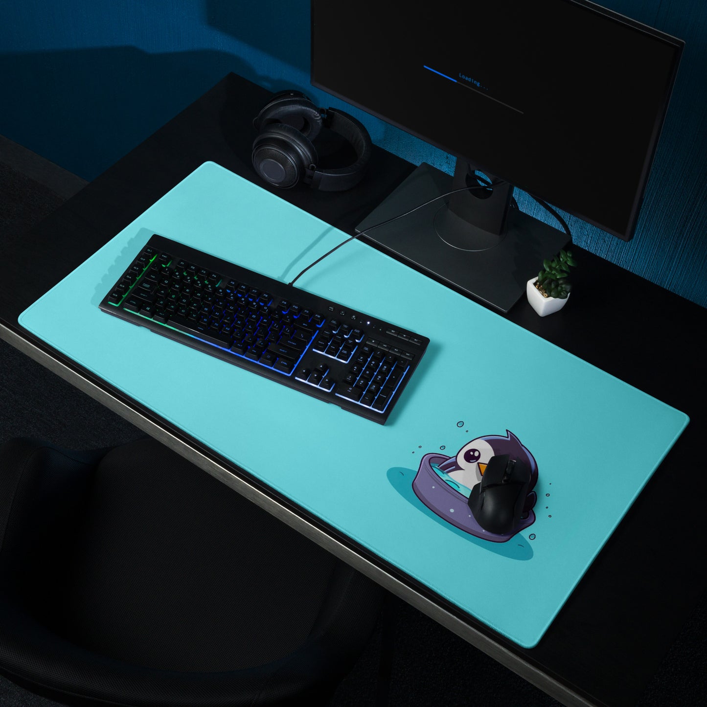 36" x 18" desk pad with a cute penguin sitting in an ice bath on it shown on a desk setup. Blue in color.