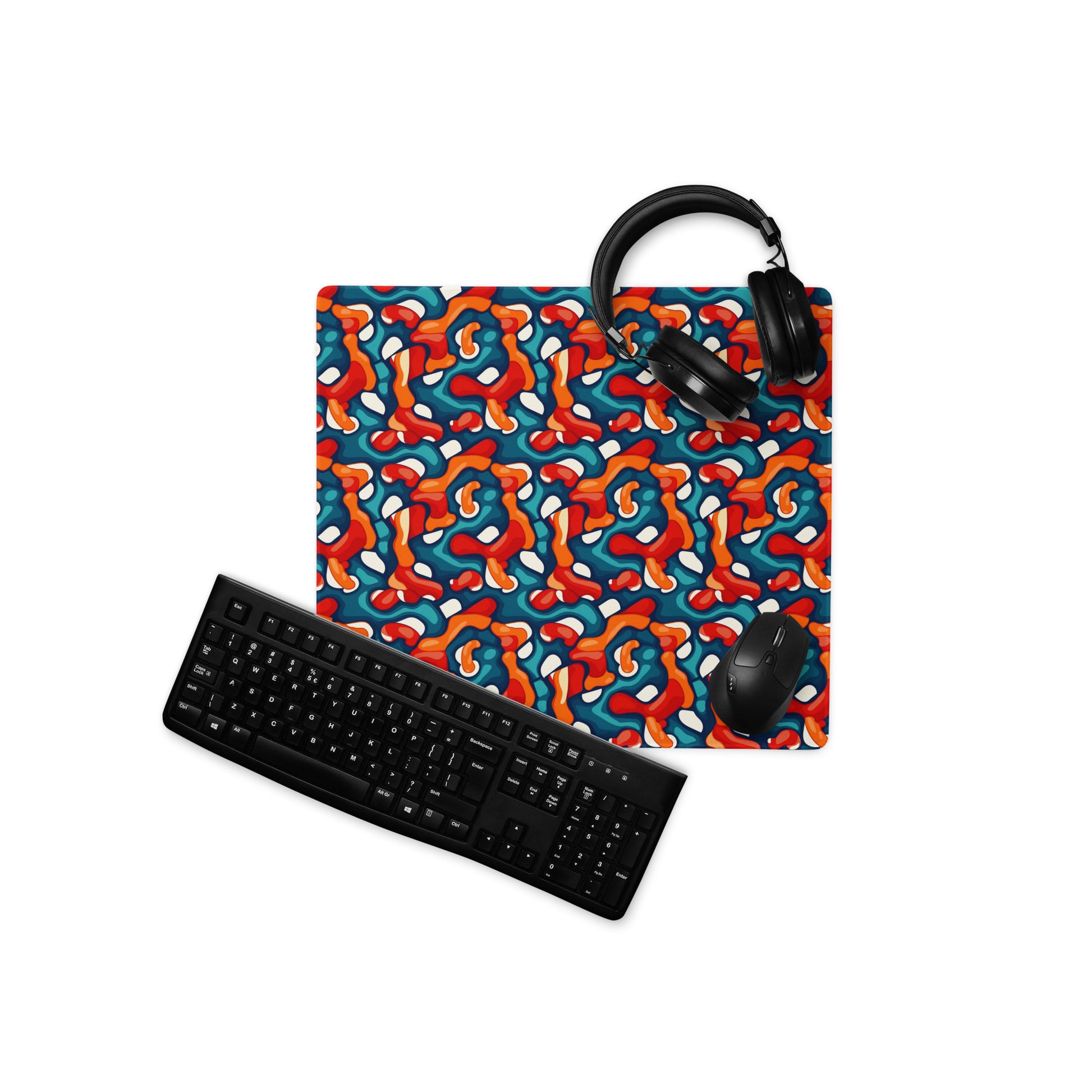 A 18" x 16" desk pad with abstract line art on it displayed with a keyboard, headphones and a mouse. Red, Teal and Orange in color.