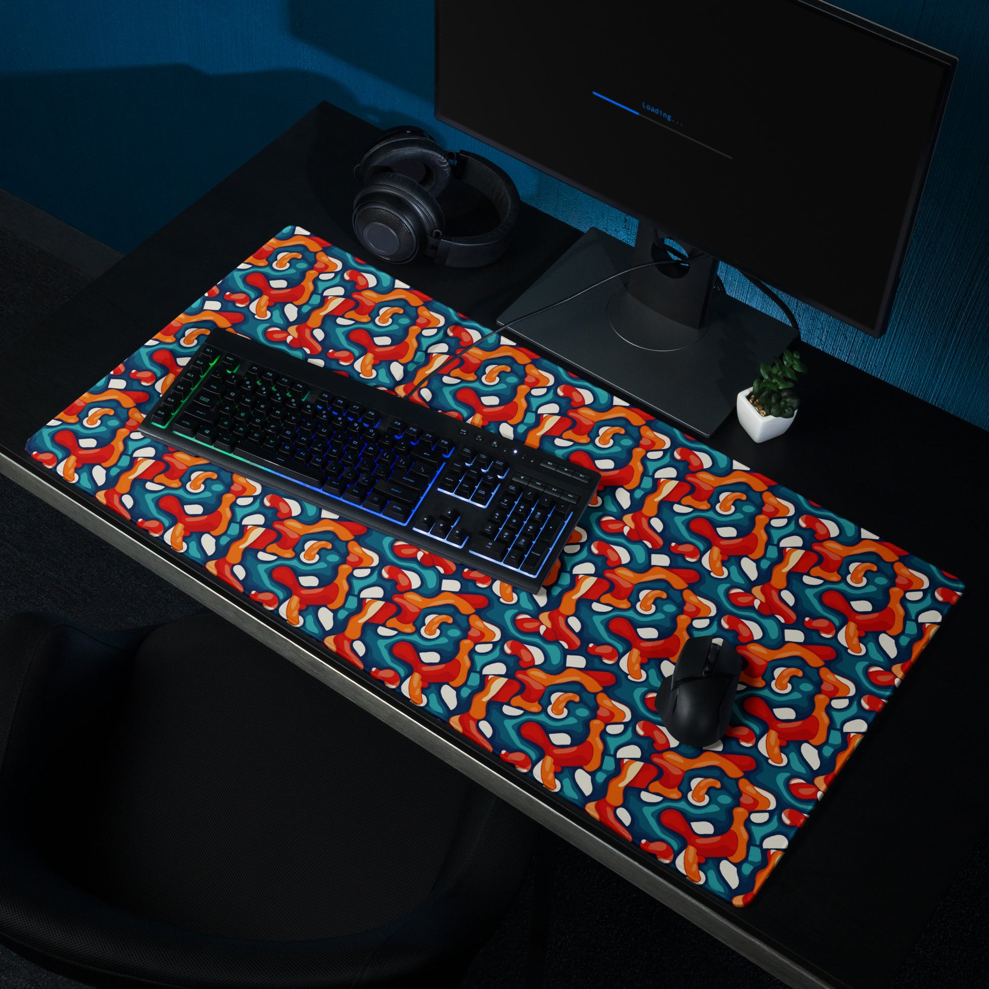 A 36" x 18" desk pad with abstract line art on it shown on a desk setup. Red, Teal and Orange in color.