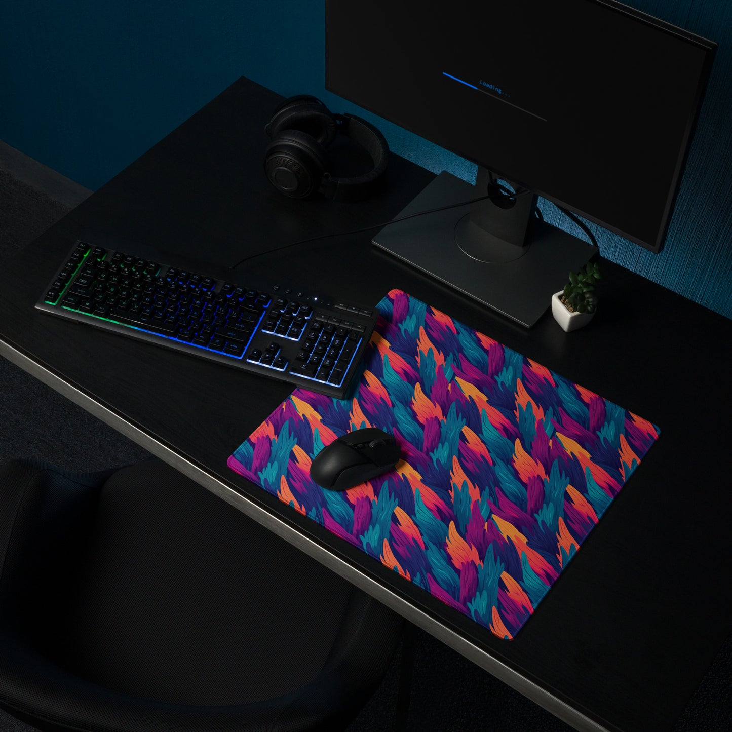 A 18" x 16" desk pad with a wavy flame pattern on it shown at a desk setup. Blue, Orange and Purple in color.