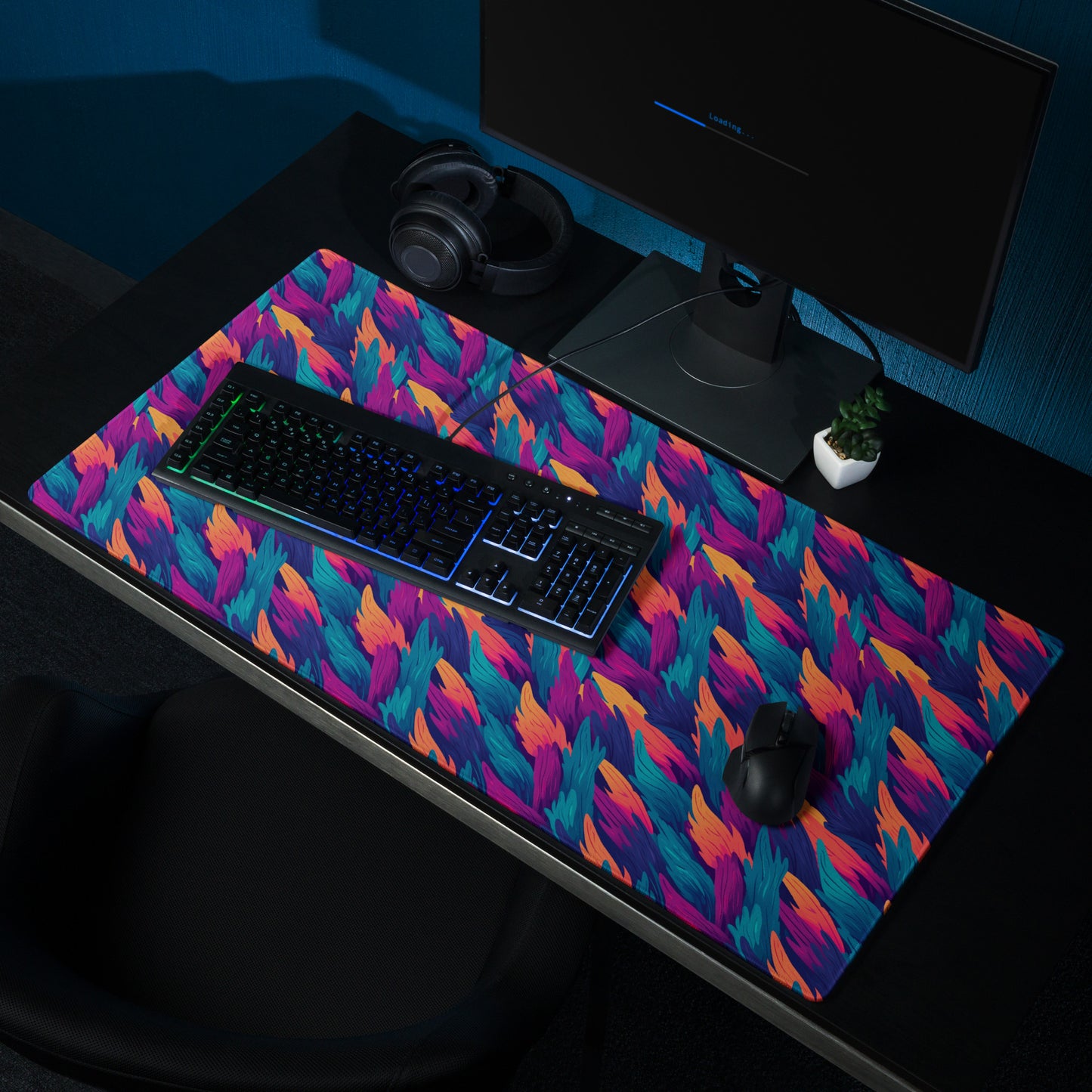 A 36" x 18" desk pad with a wavy flame pattern on it shown on a desk setup. Blue, Orange and Purple in color.