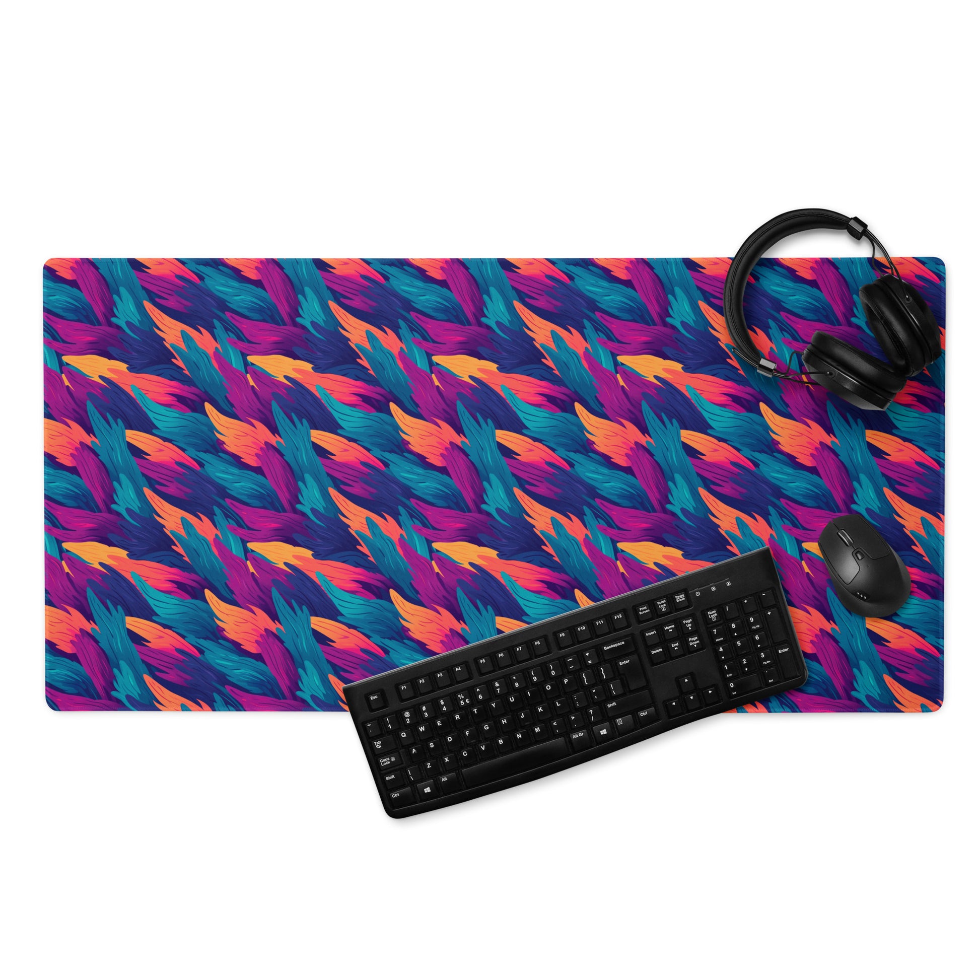 A 36" x 18" desk pad with a wavy flame pattern on it displayed with a keyboard, headphones and a mouse. Blue, Orange and Purple in color.