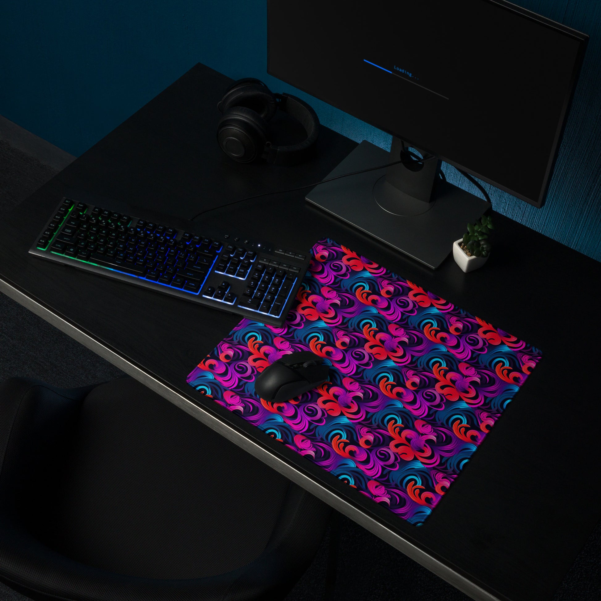 An 18" x 16" desk pad with a bright floral pattern all over it shown on a desk setup. Blue, Purple and Red in color.