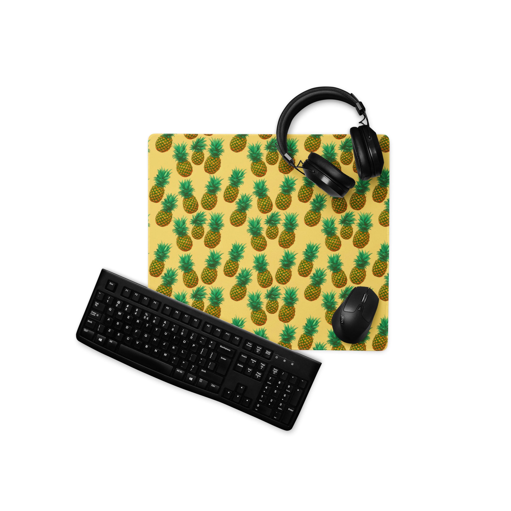 A 18" x 16" desk pad with pineapples all over it displayed with a keyboard, headphones and a mouse. Yellow in color.