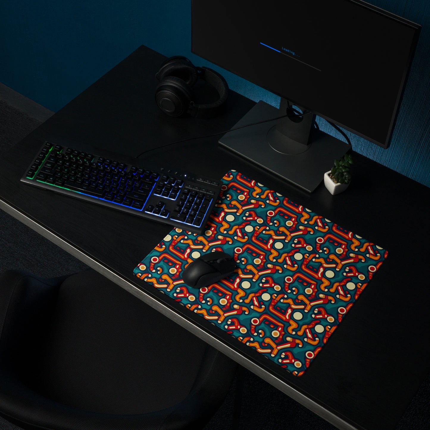 A 18" x 16" desk pad with abstract line art on it shown on a desk setup. Red, Orange and Teal in color.