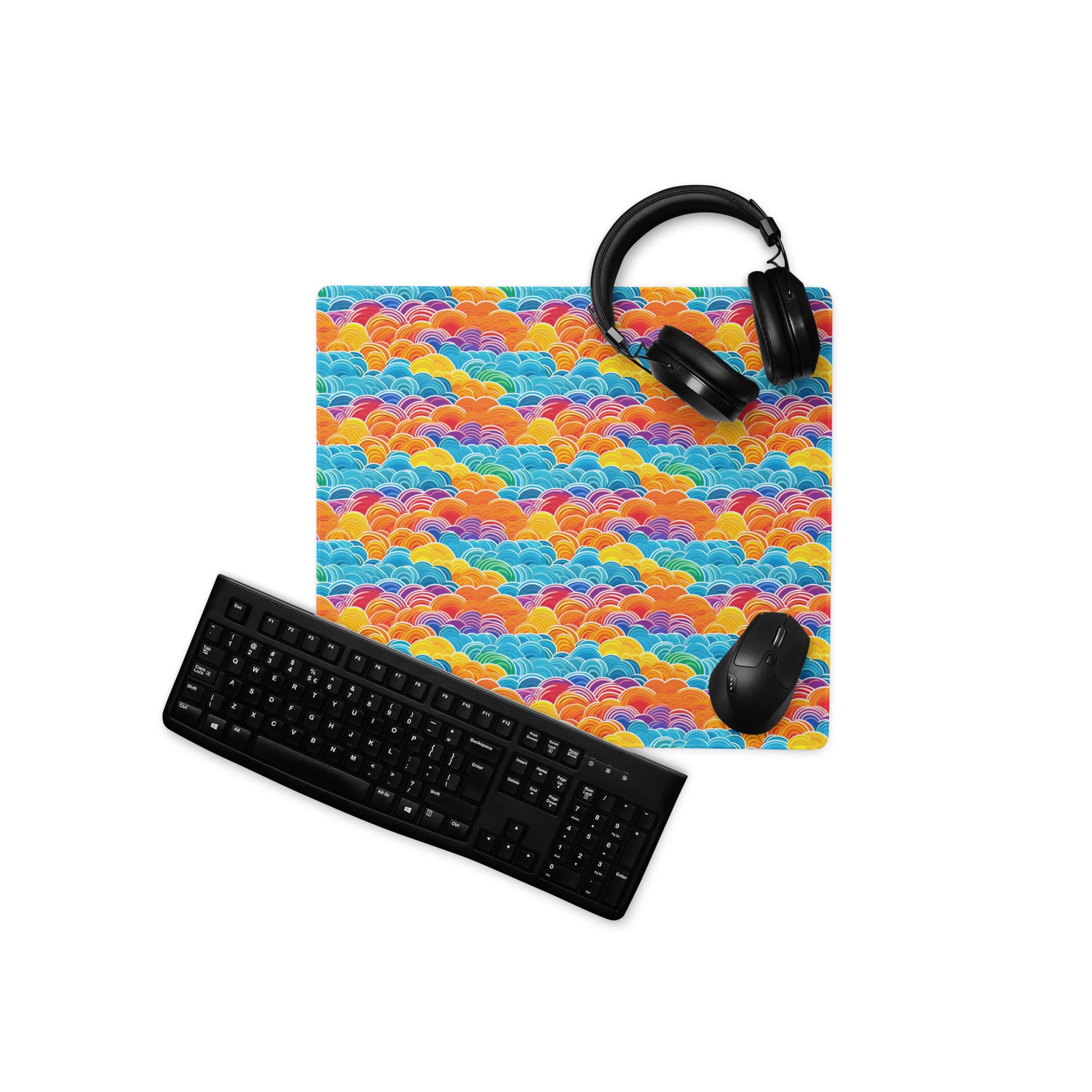 An 18" x 16" desk pad with bubbly swirly clouds all over it displayed with a keyboard, headphones and a mouse on it. Rainbow colored.