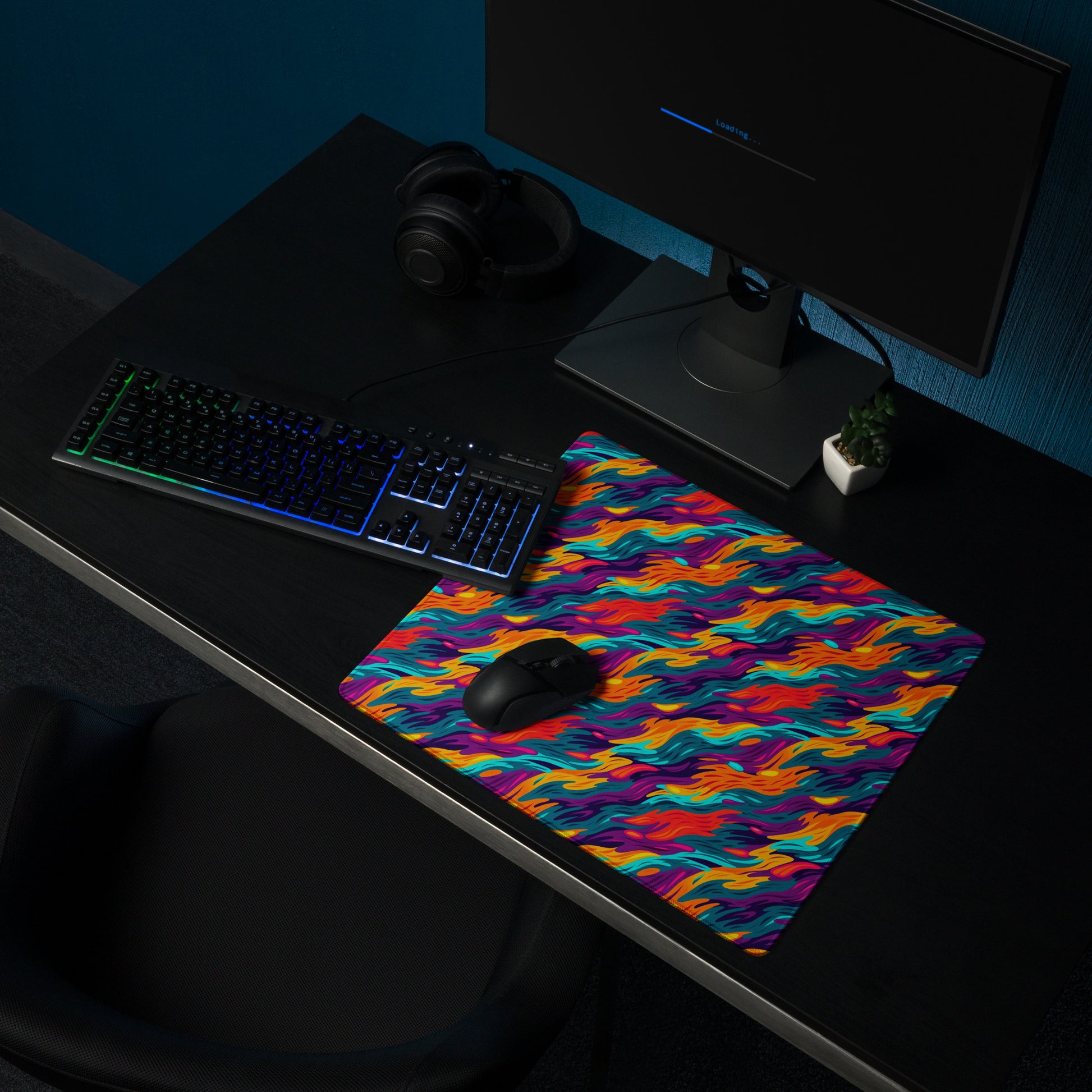 An 18" x 16" desk pad with a wavy flame pattern on it shown on a desk setup. Rainbow in color.