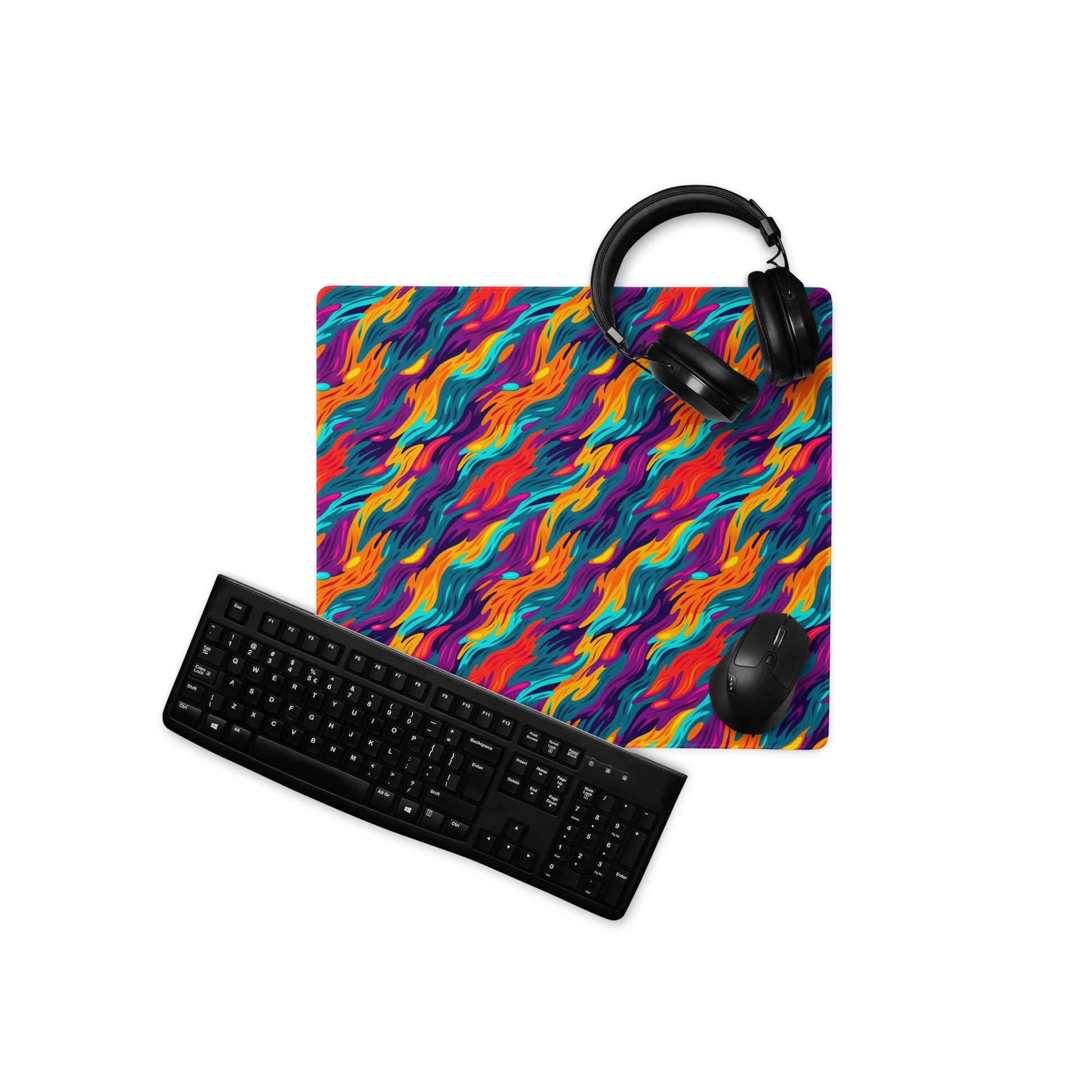An 18" x 16" desk pad with a wavy flame pattern on it displayed with a keyboard, headphones and a mouse. Rainbow in color.
