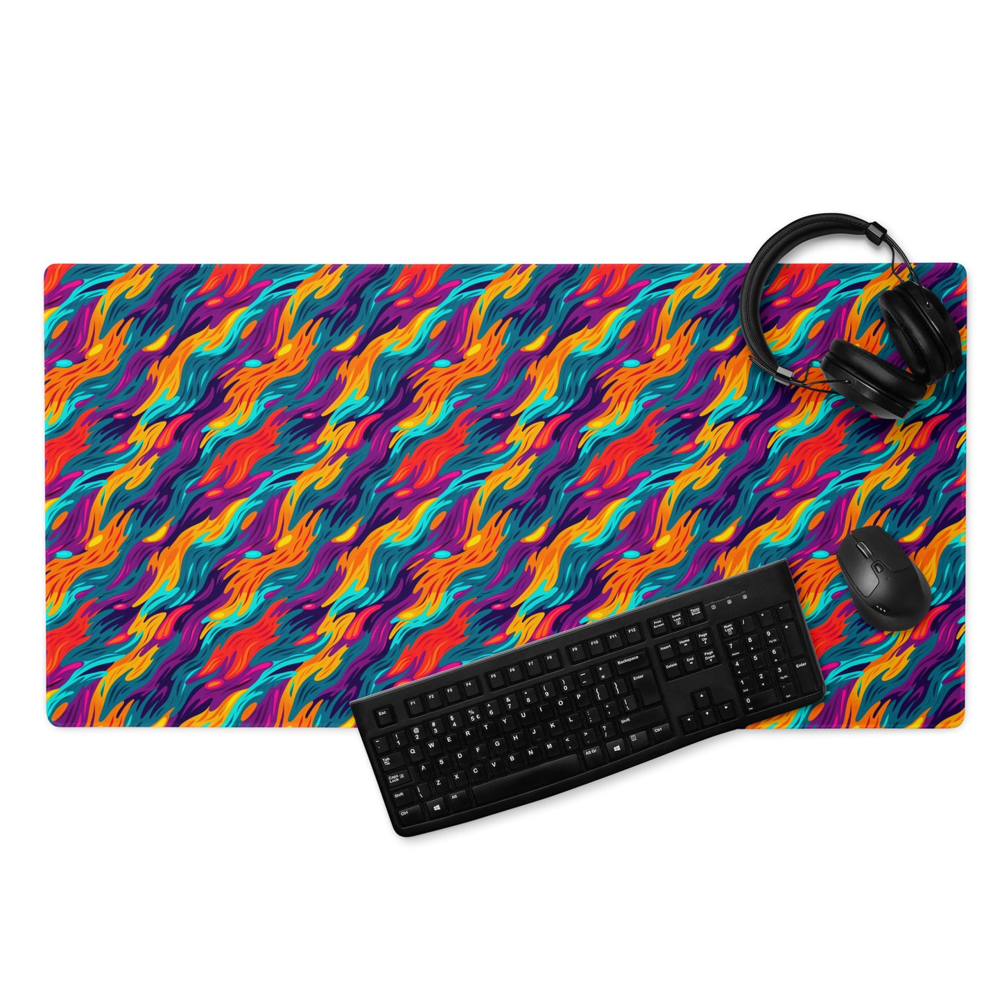 A 36" x 18" desk pad with a wavy flame pattern on it displayed with a keyboard, headphones and a mouse. Rainbow in color.