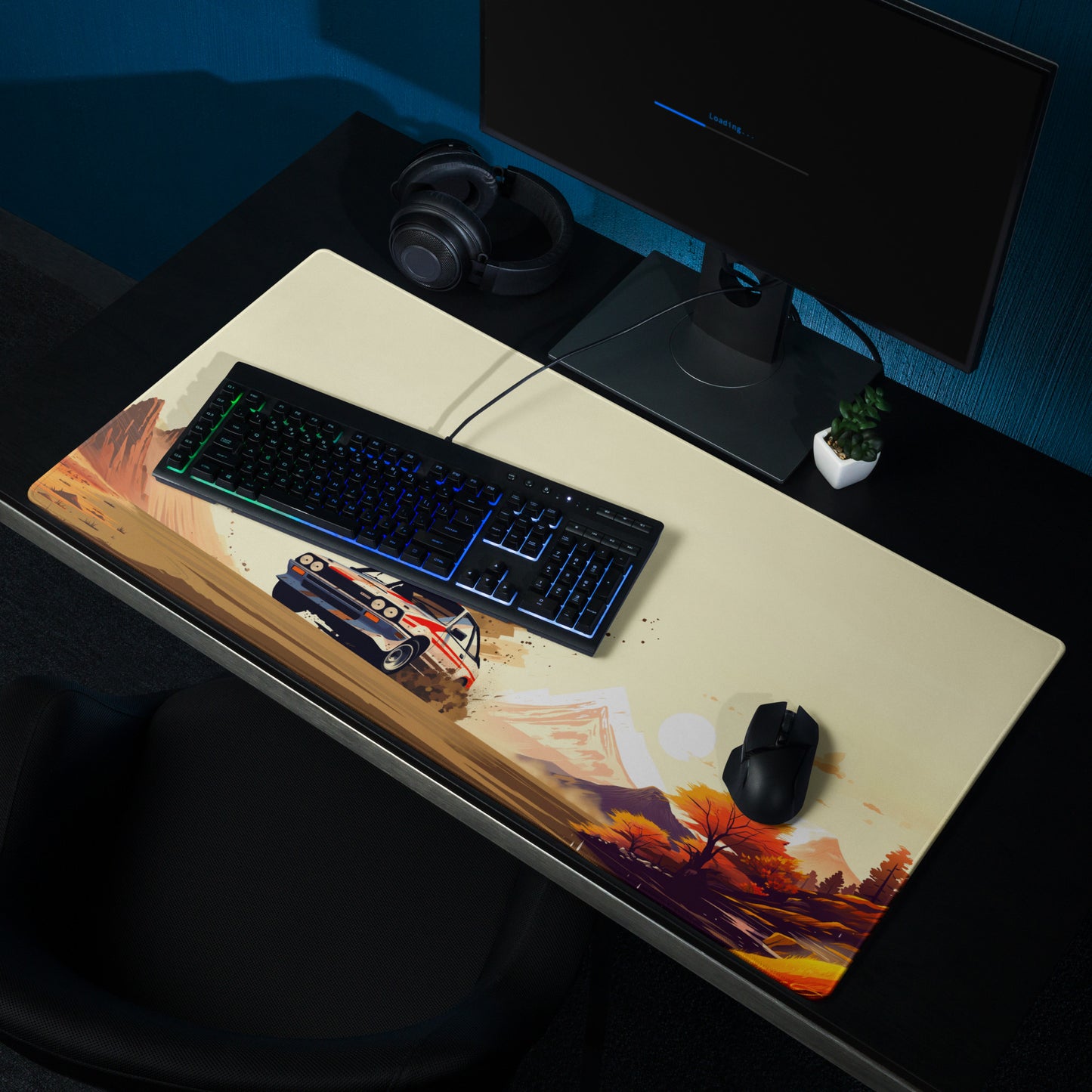 A 36" x 18" gaming desk pad with a Rally car racing through the desert shown at a desk setup. Brown and Beige in Color.