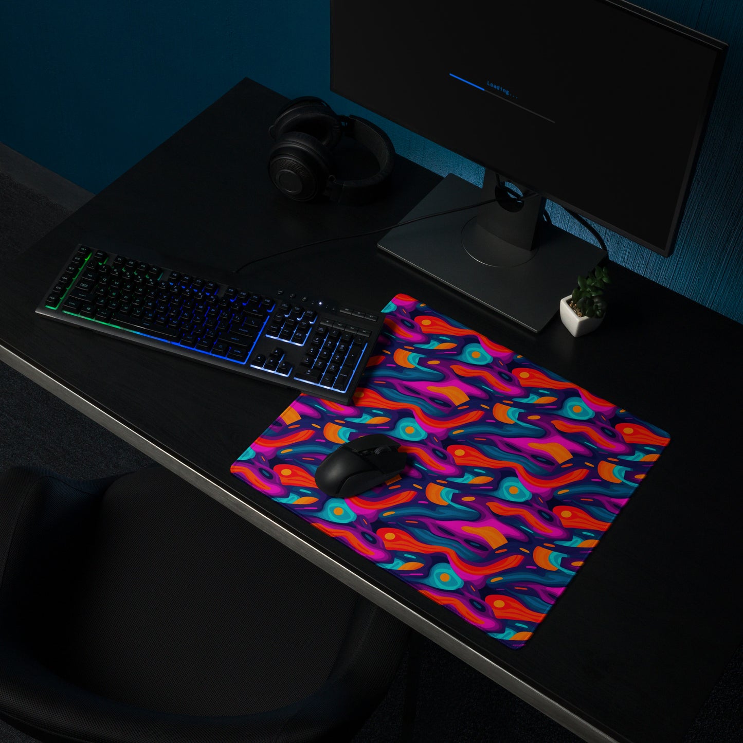A 18" x 16" desk pad with a wavy abstract pattern on it shown on a desk setup. Blue, Purple and Red in color.