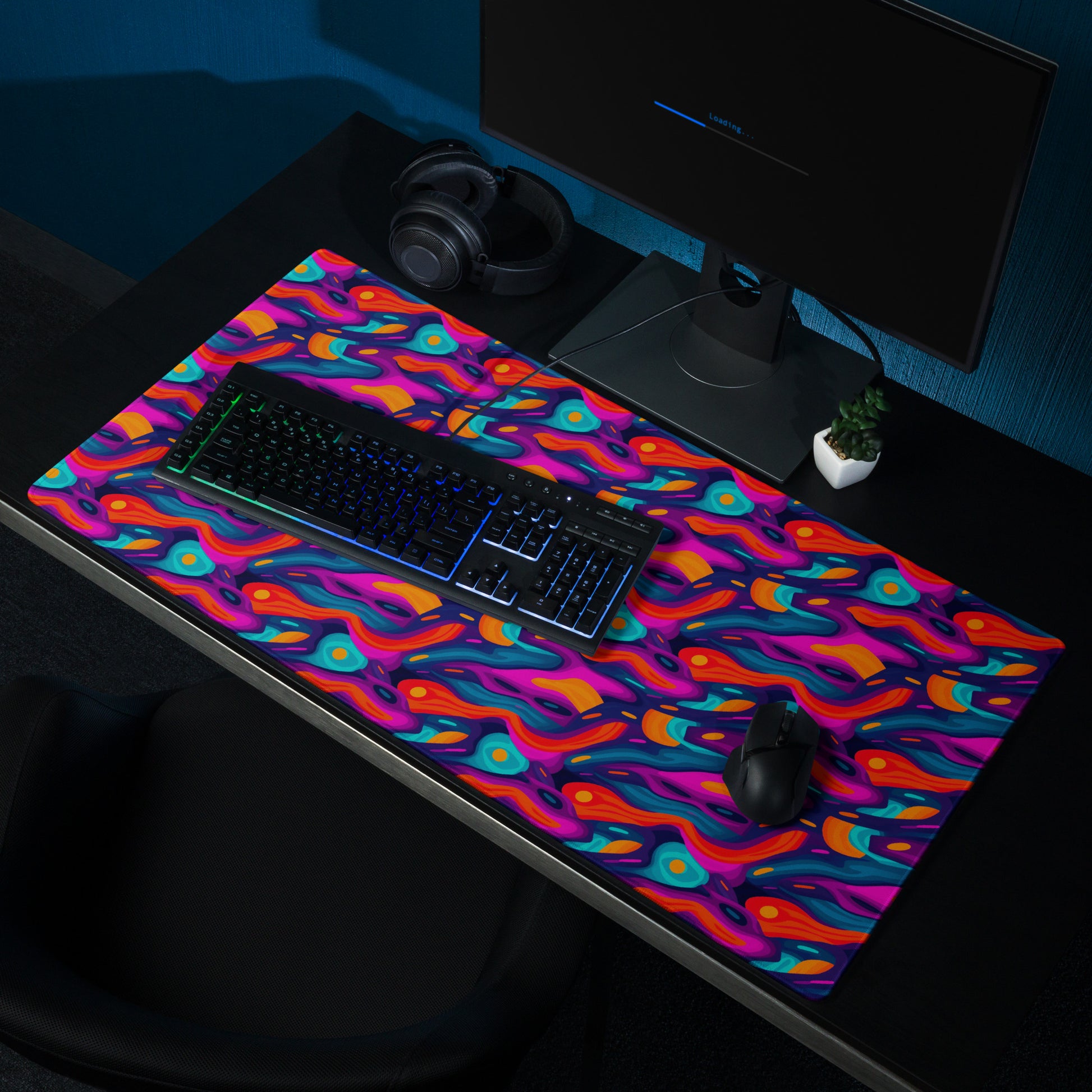 A 36" x 18" desk pad with a wavy abstract pattern on it shown on a desk setup. Blue, Purple and Red in color.