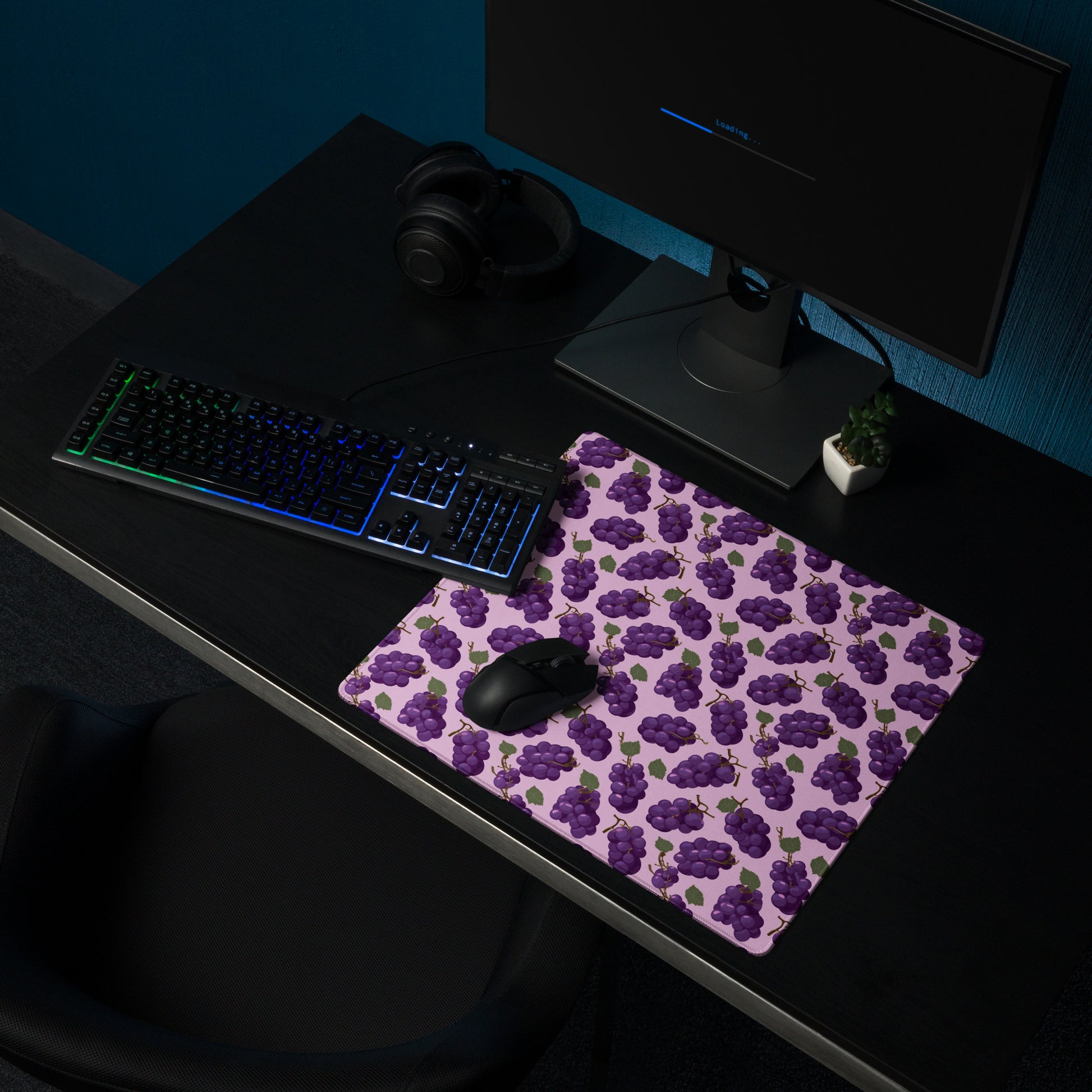 A 18" x 16" desk pad with bushels of grapes all over it shown on a desk setup. Purple in color.