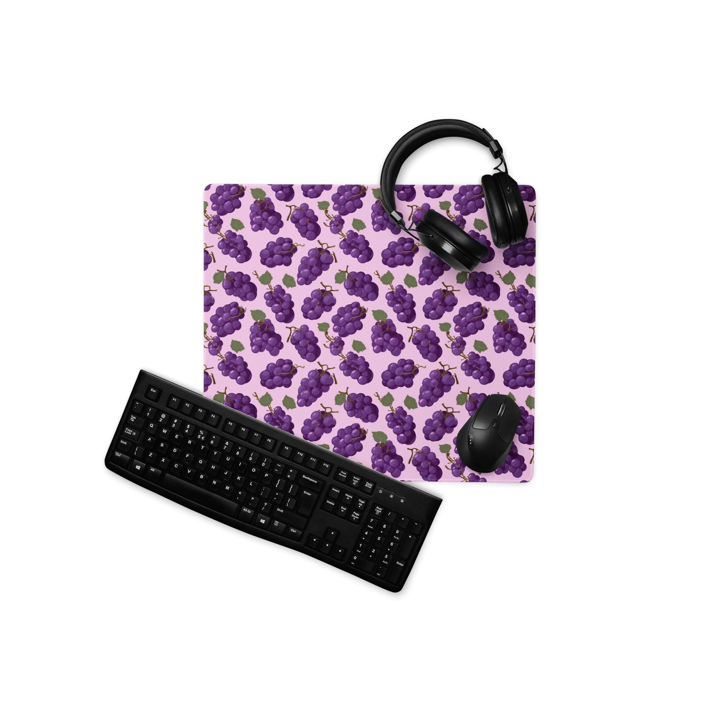 A 18" x 16" desk pad with bushels of grapes all over it displayed with a keyboard, headphones and a mouse. Purple in color.