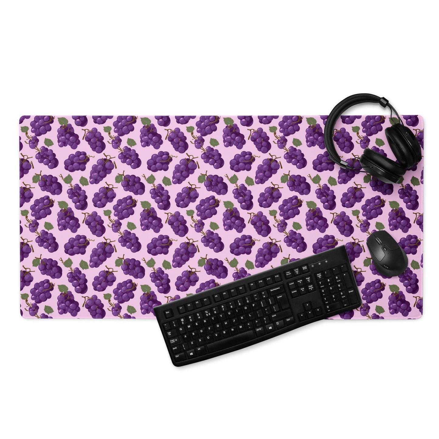 A 36" x 18" desk pad with bushels of grapes all over it displayed with a keyboard, headphones and a mouse. Purple in color.