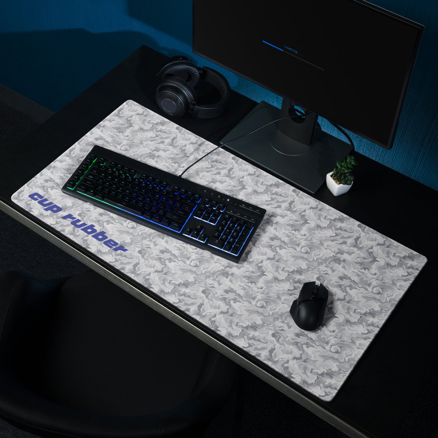 A 36" x 18" desk pad with a camo pattern and the word "Cup Rubber" on it in the bottom left corner shown on a desk setup. Beige and White in color.