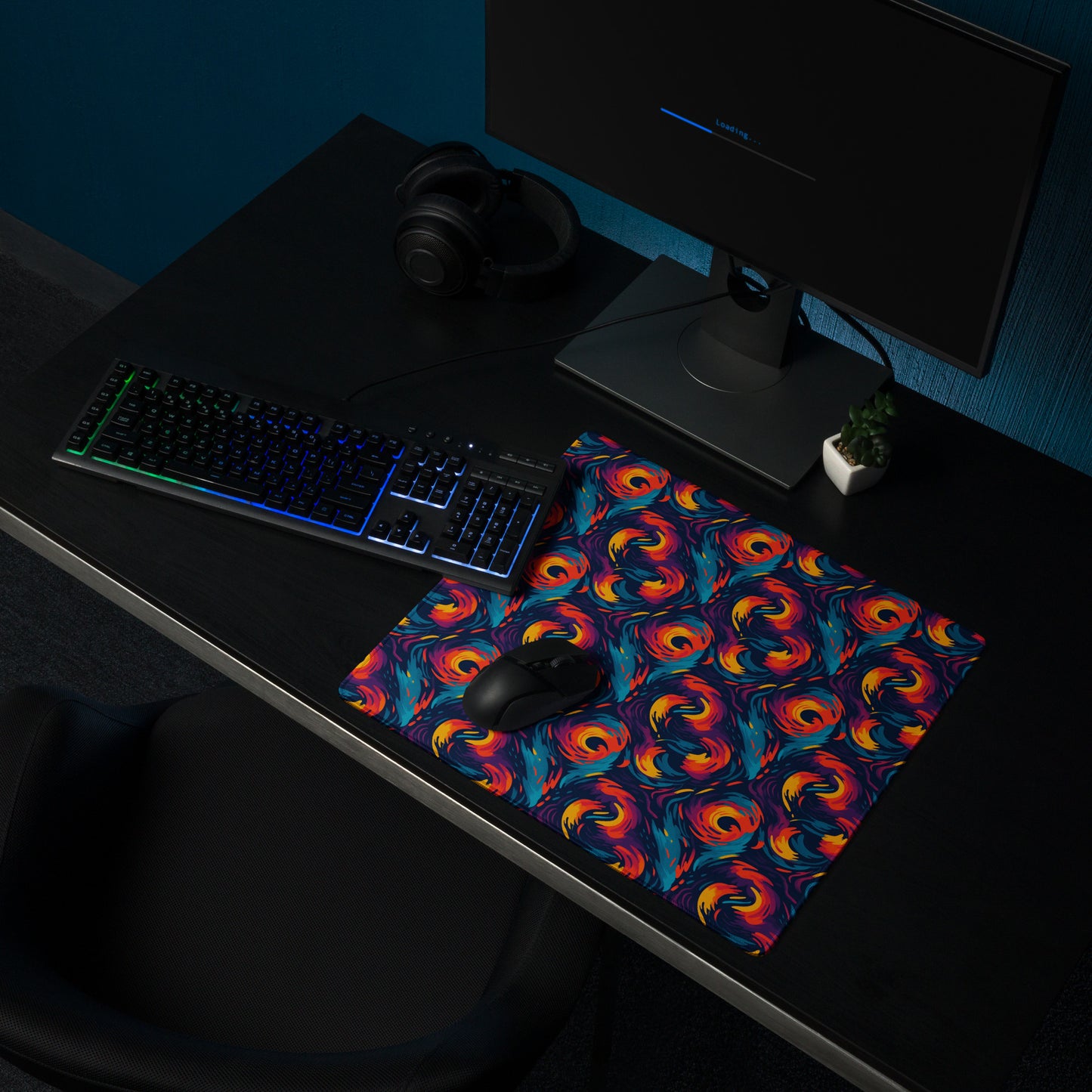 A 18" x 16" desk pad with fiery swirls on it shown on a desk setup. Red and Blue in color.