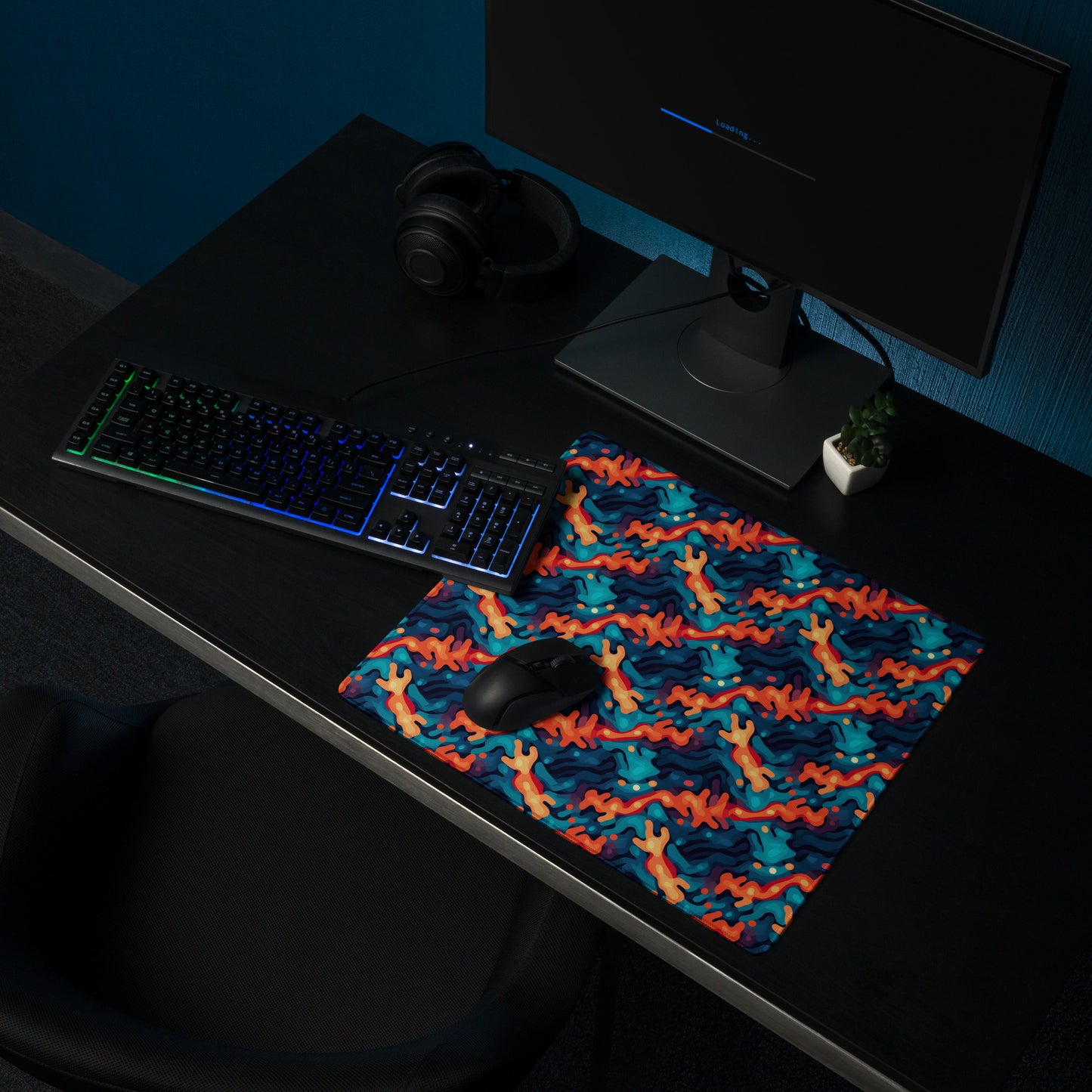 A 18" x 16" desk pad with a wavy woven pattern on it shown on a desk setup. Red and Blue in color.