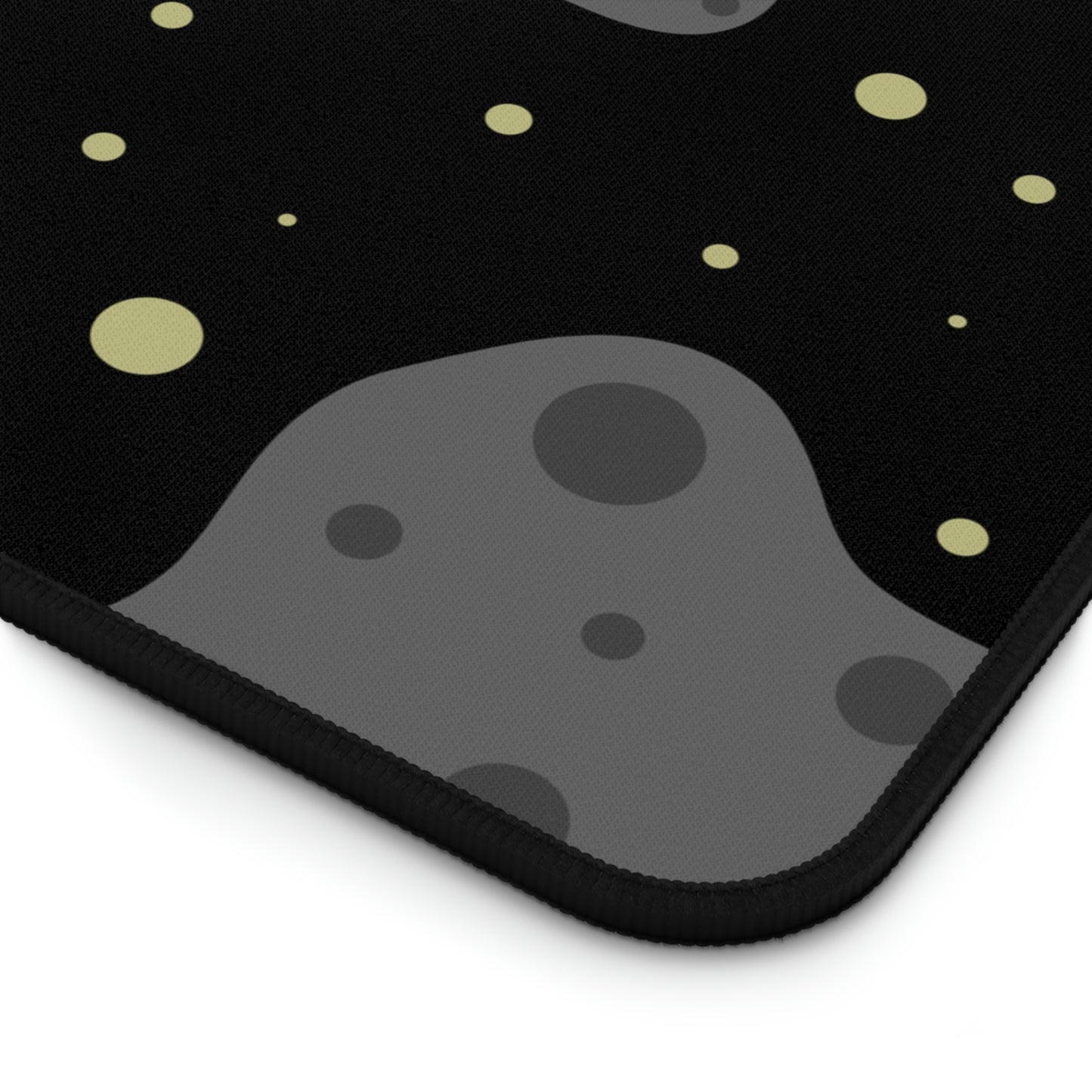 The corner of a 12" x 18" desk mat with a black background, gray asteroids, and yellow stars.